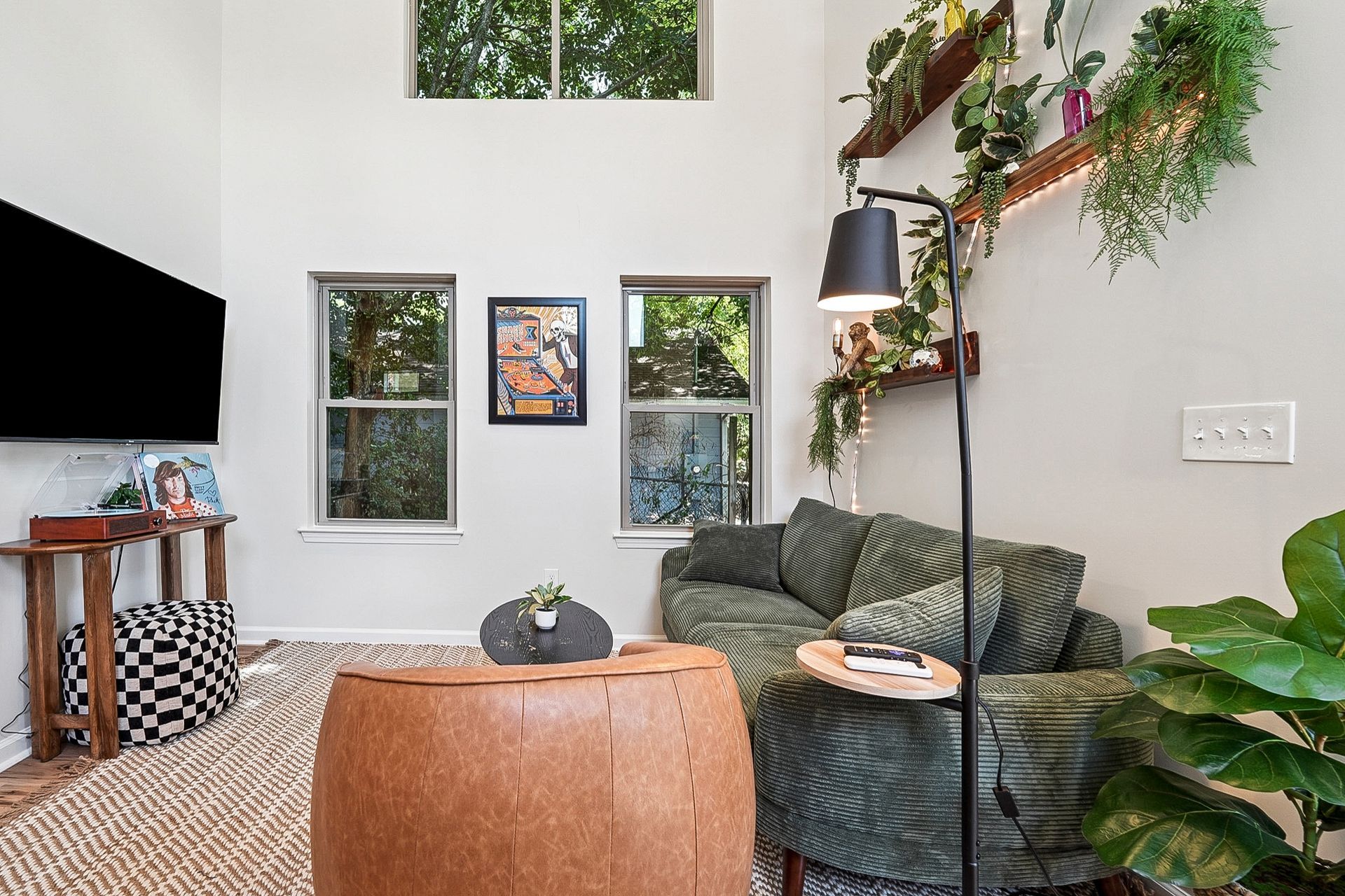 Cozy living room with green plush chair, wooden table, and plants by the windows.