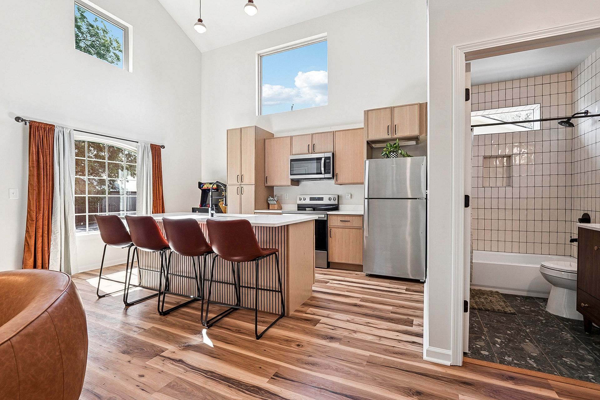 Modern kitchen with island seating, stainless steel appliances, and a partially visible bathroom.