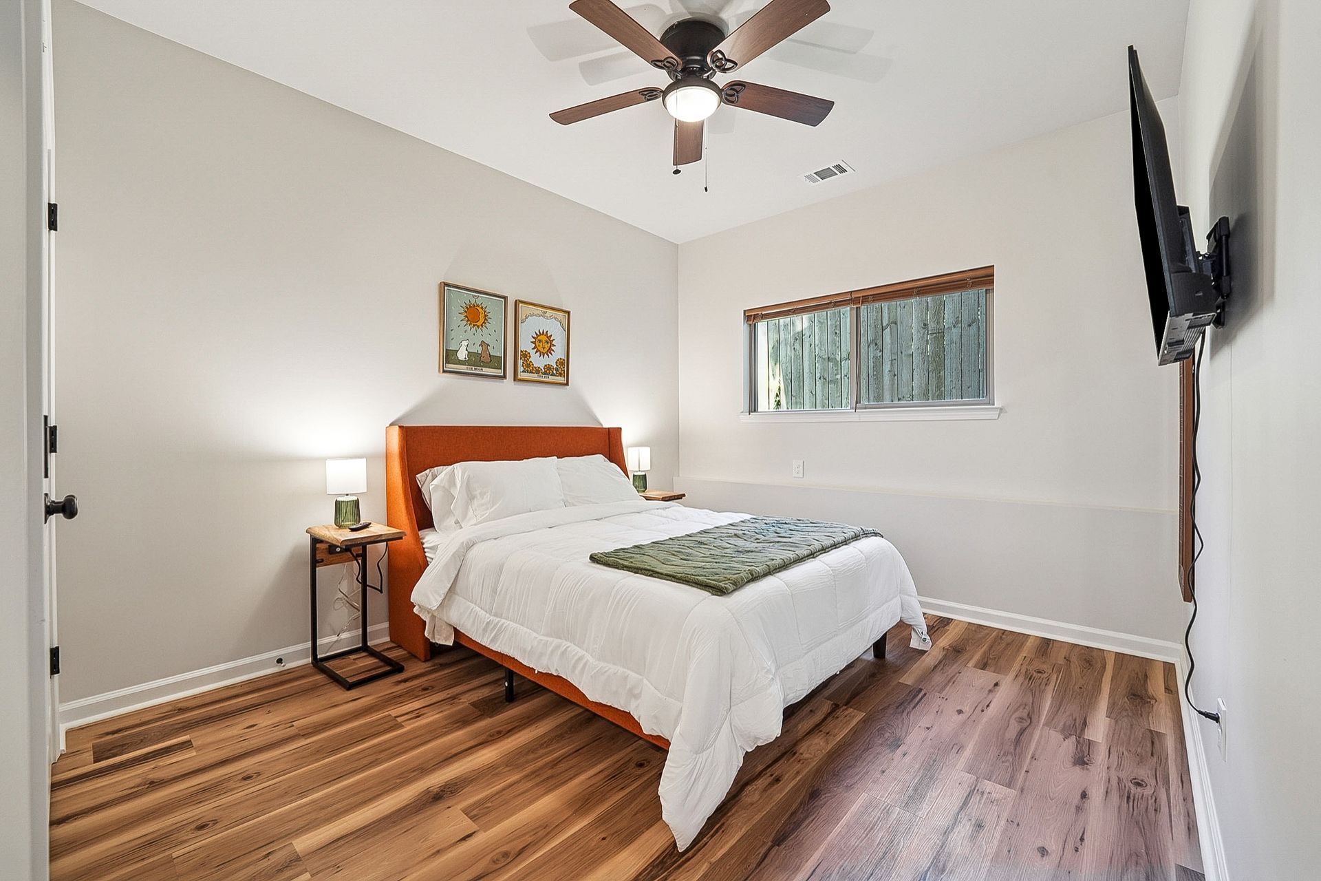 Bedroom with bed, nightstands, TV, and ceiling fan. Wooden floors and neutral walls.