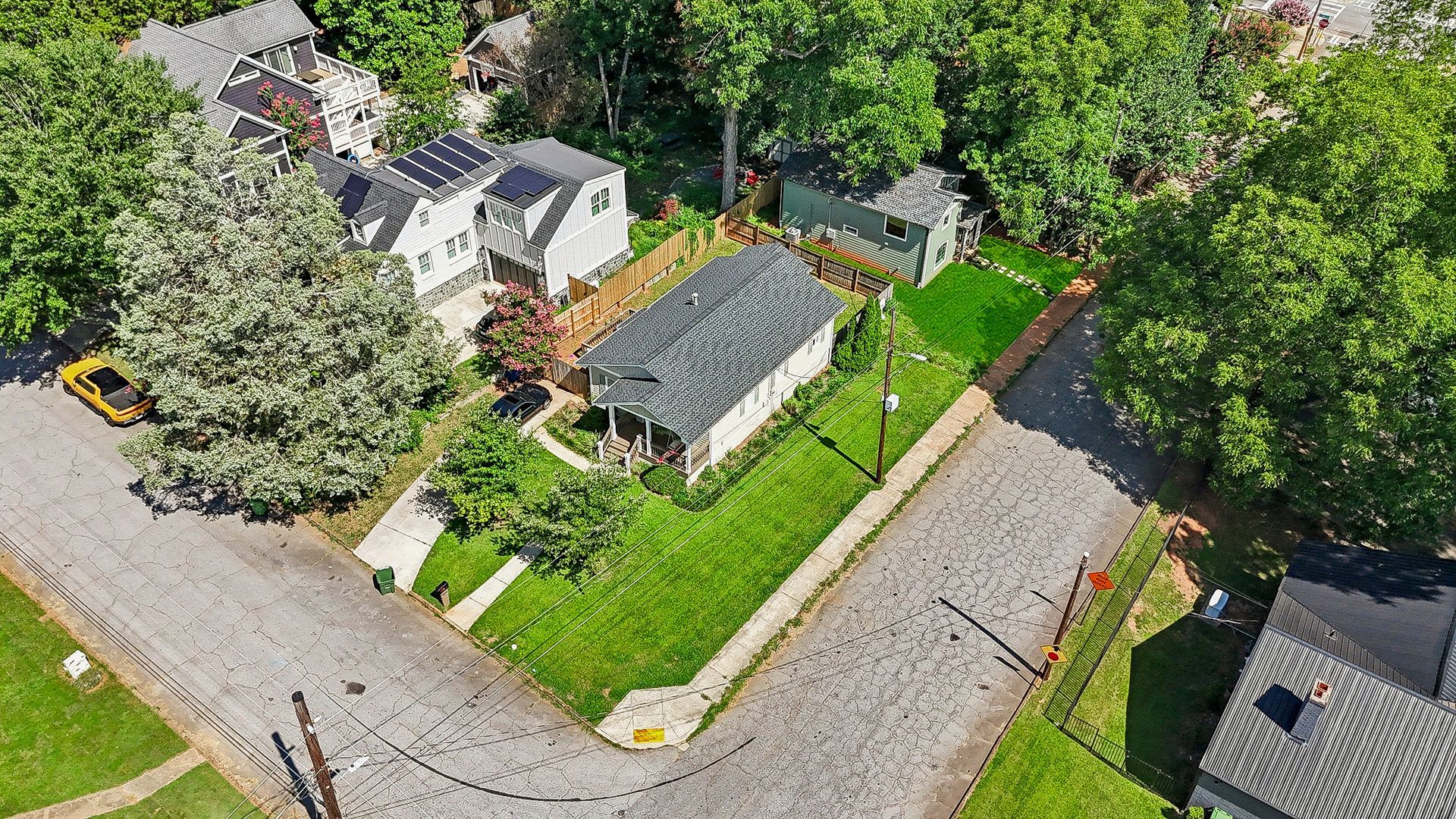 Aerial view of a house with green lawn, surrounded by trees and a street.