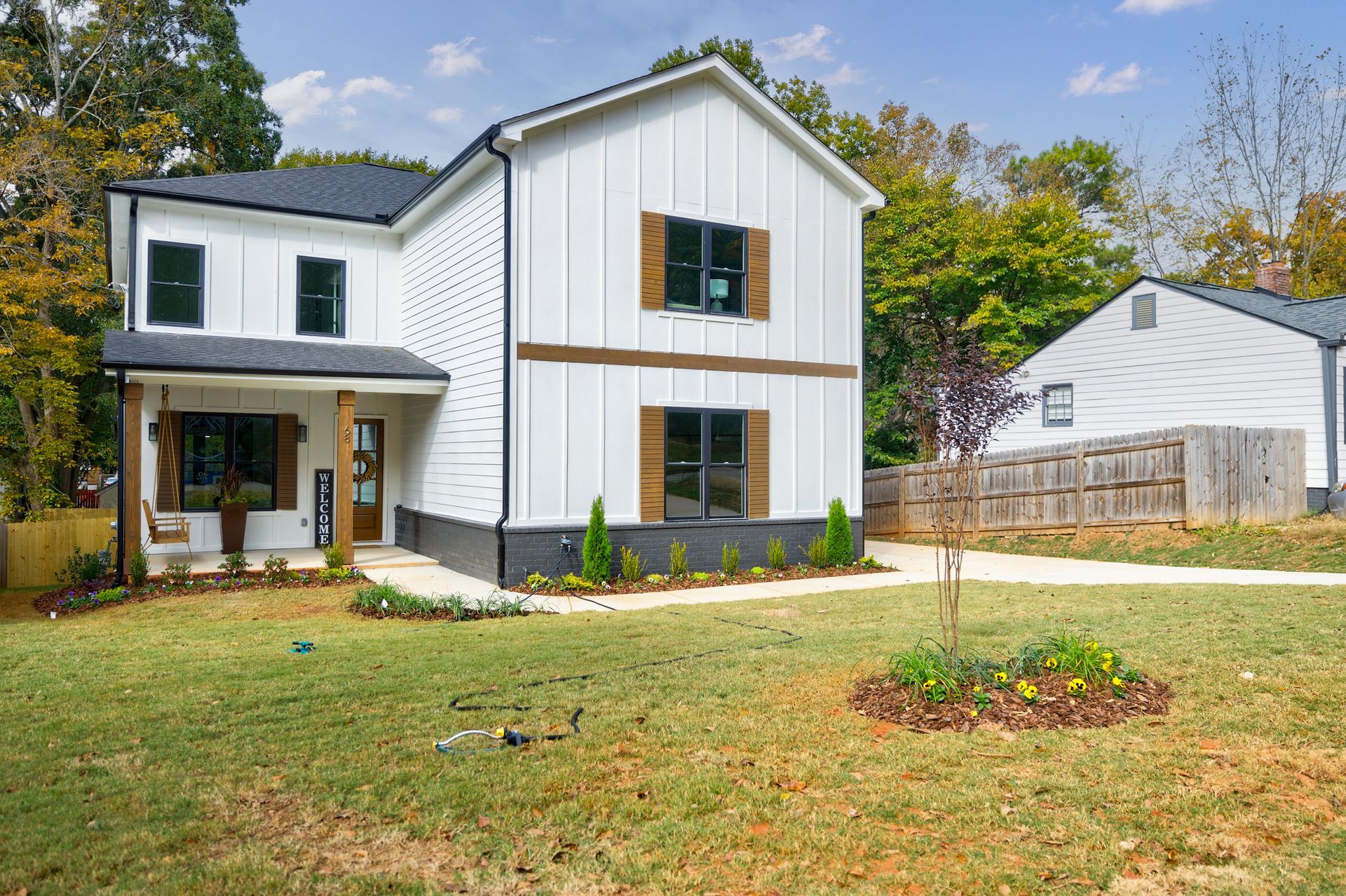 White two-story house with black roof and shutters, brown accents, and a small front yard.
