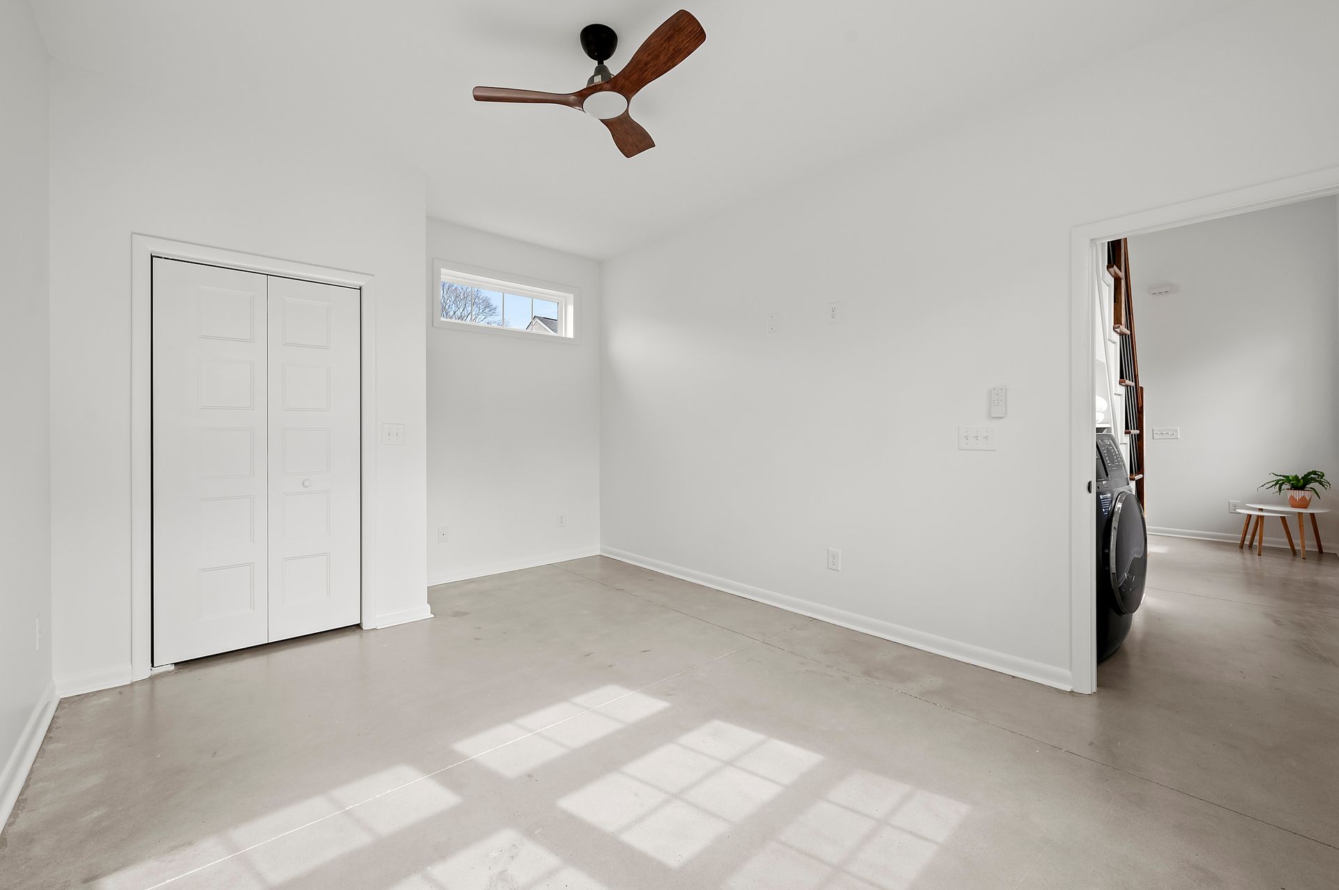Empty room with white walls, closet, and ceiling fan; a glimpse into another room on the right.