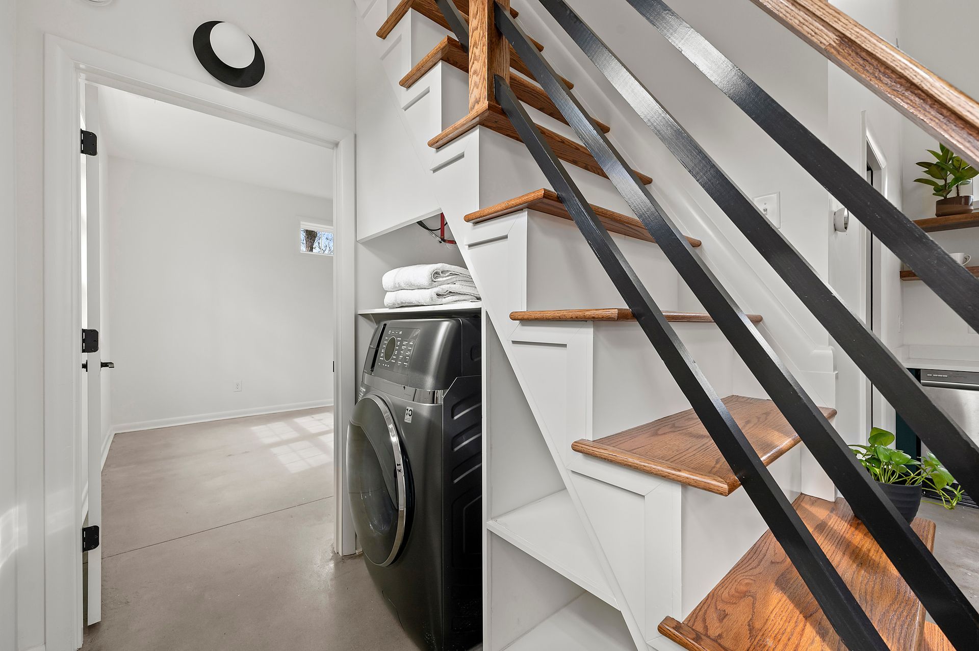 Laundry room with a washing machine under a staircase with wood and black metal railing.