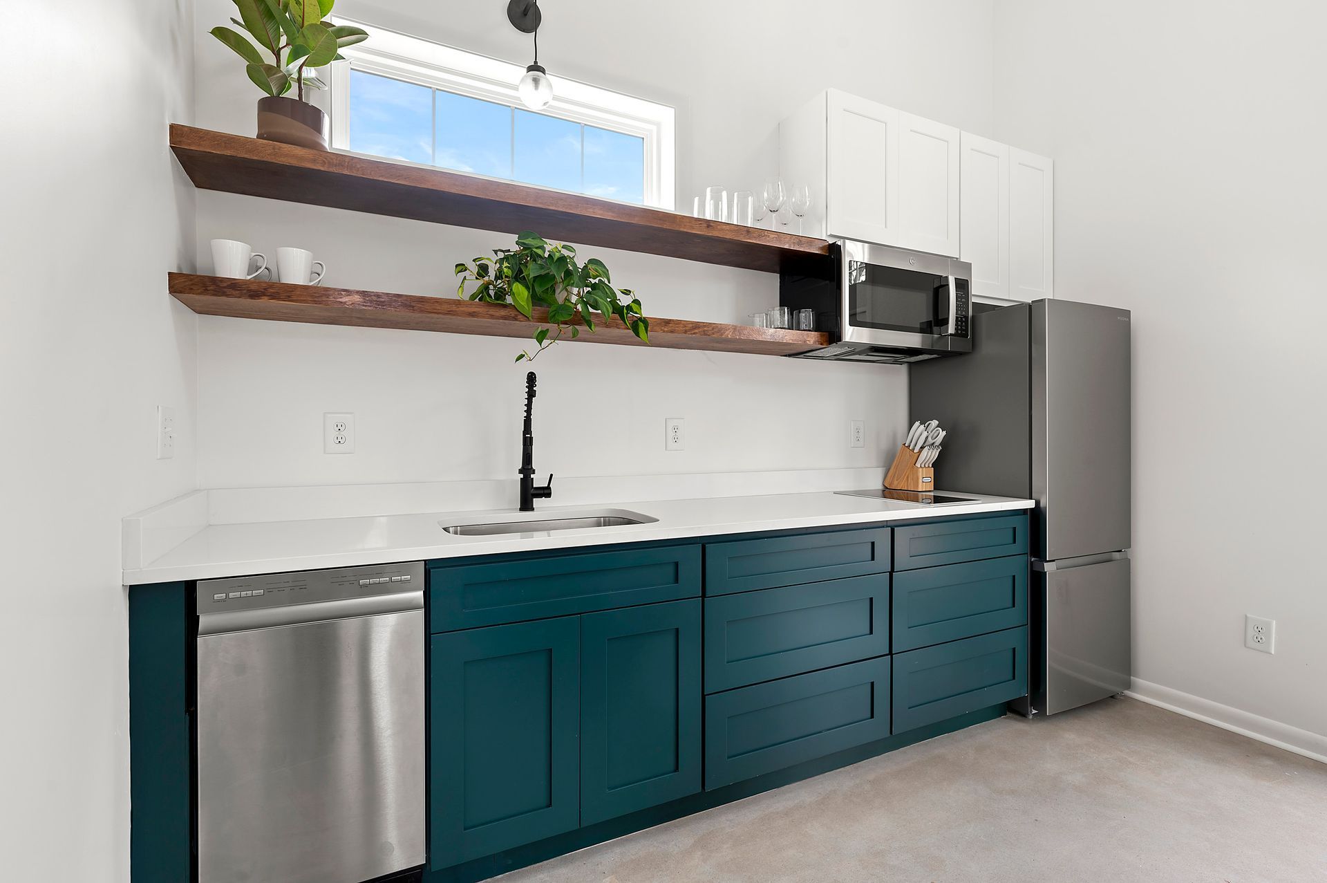 Modern kitchenette with teal cabinets, stainless steel appliances, and wooden shelves.