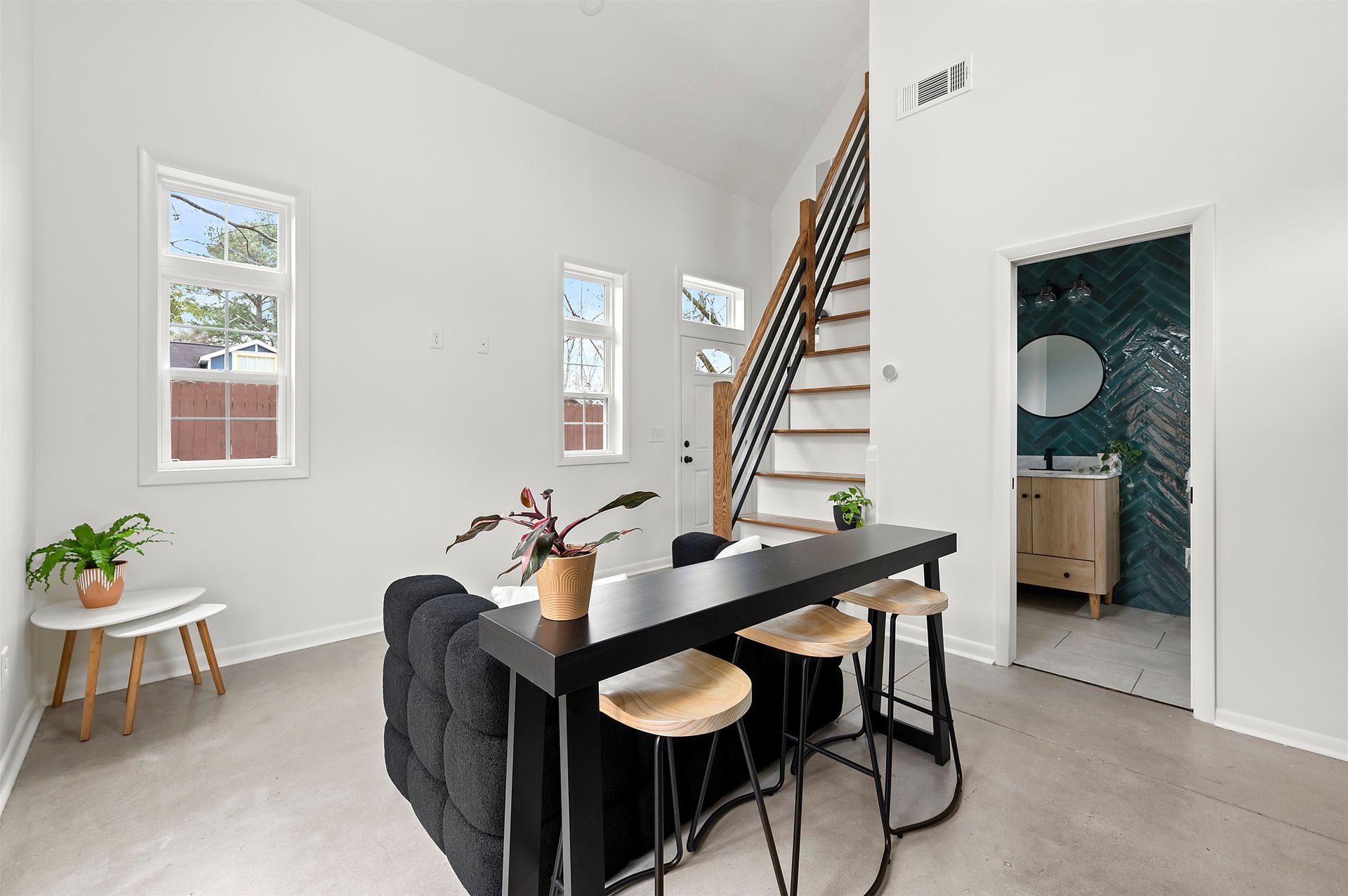 Modern living area with black bar, stools, staircase, windows, and bathroom.