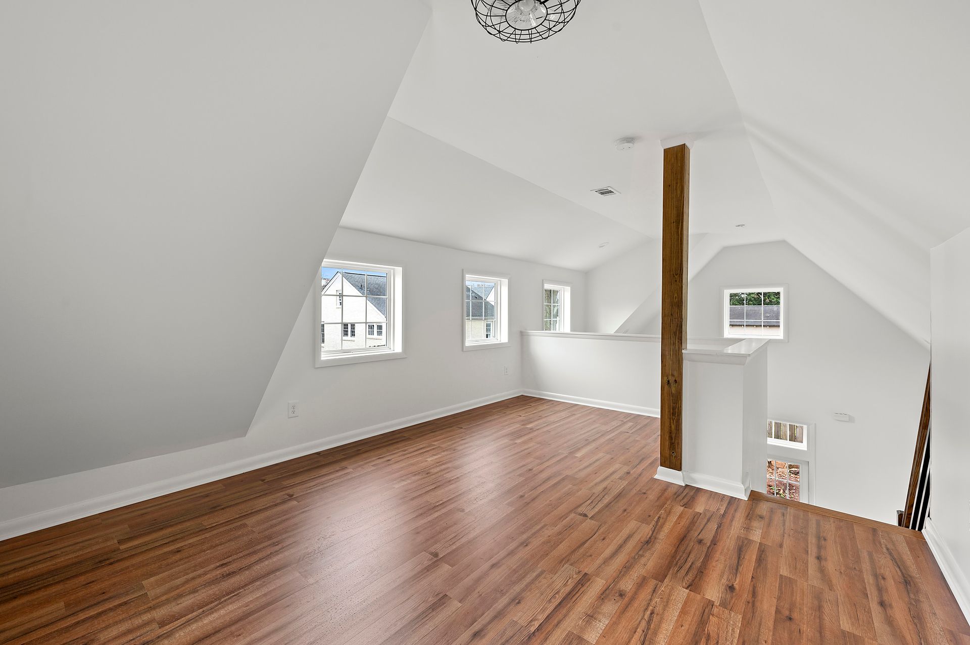 Loft room with hardwood floors, white walls, multiple windows, and a decorative ceiling fixture.
