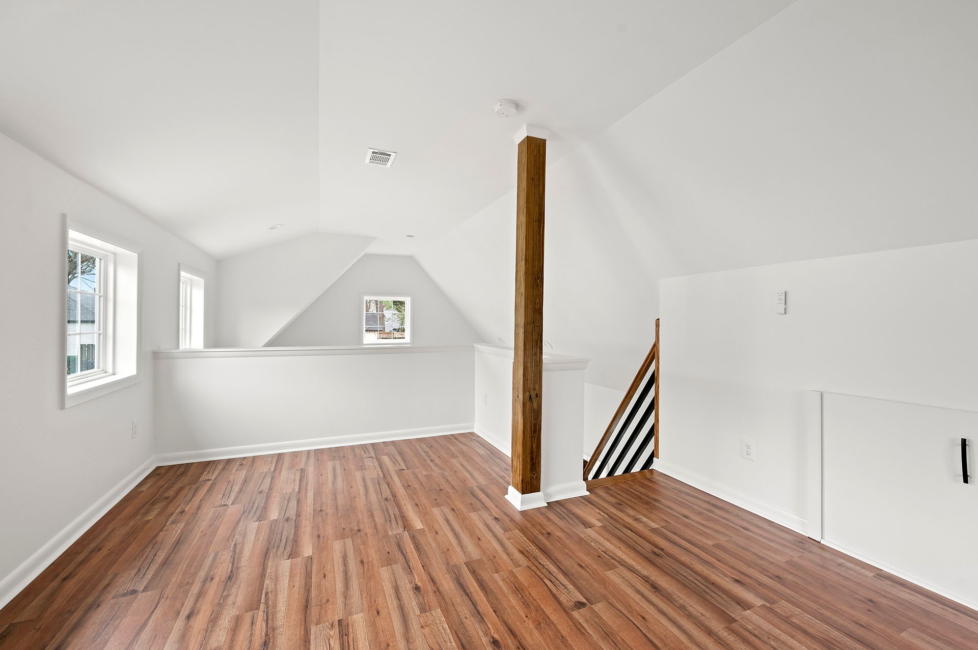 Bright, empty room with wood floors and white walls. A large wooden beam is centered.