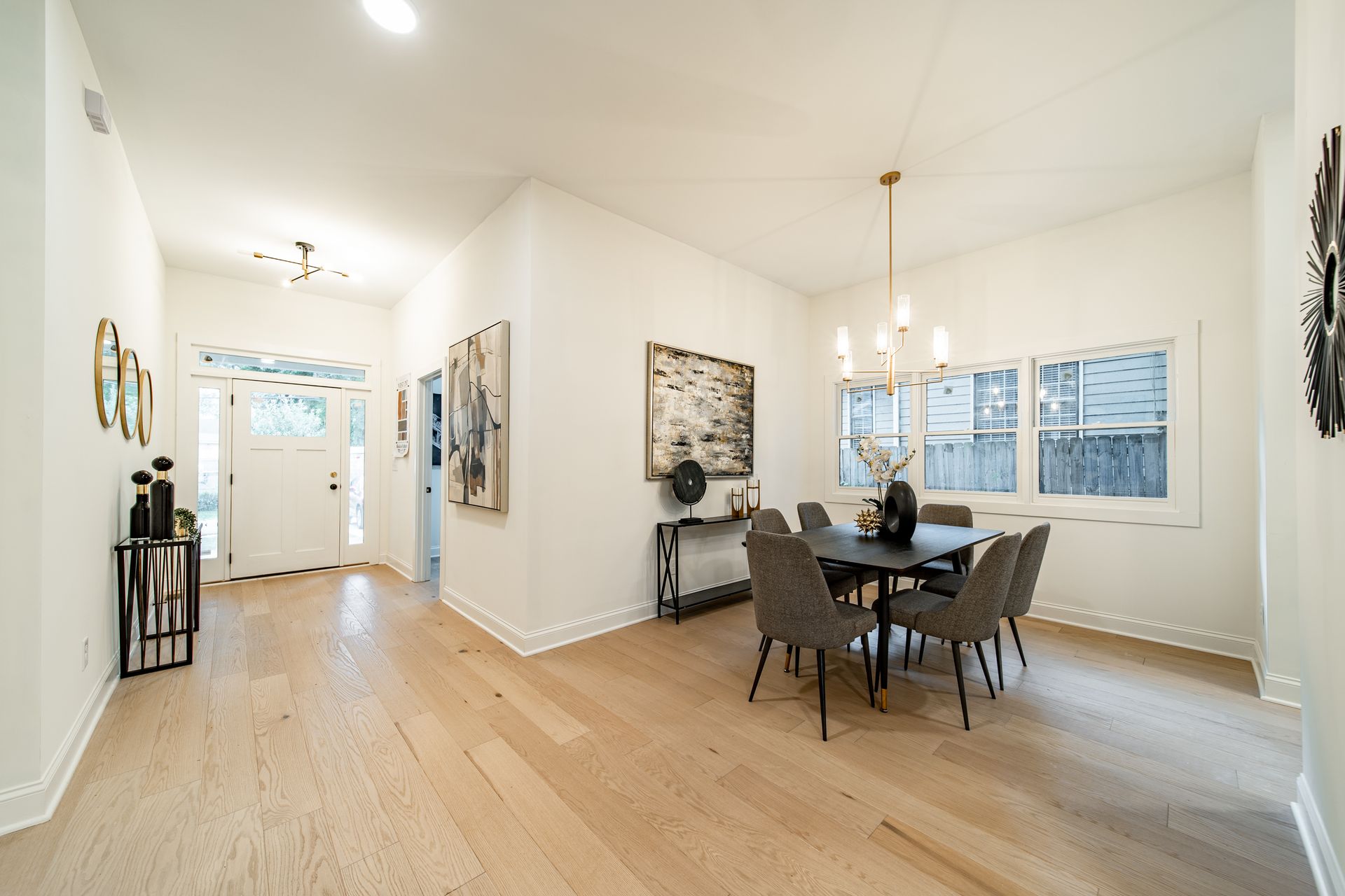 Bright dining room with a table and chairs, hardwood floor, white walls, and a decorative light fixture.