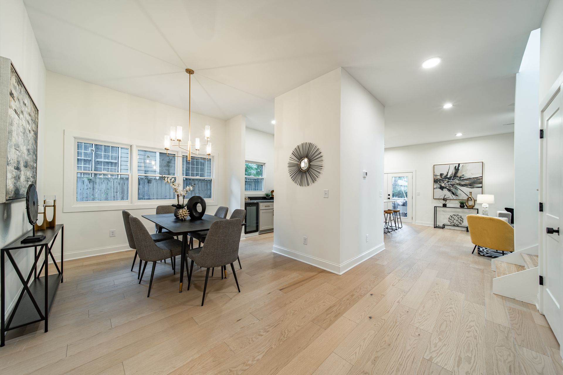 Spacious, light-filled dining room with a table, chairs, and chandelier. Wooden floors and white walls.