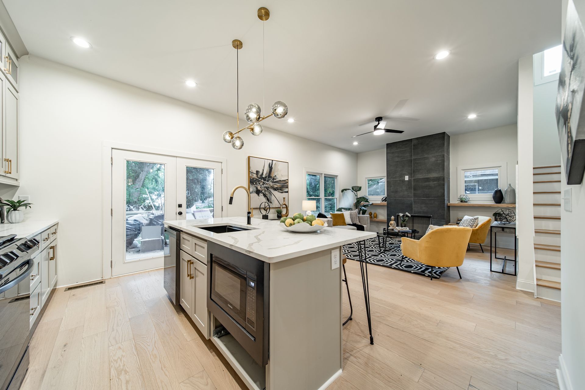 Modern open-concept kitchen with island, seating area, and French doors to a patio. Bright, light wood floors and white walls.