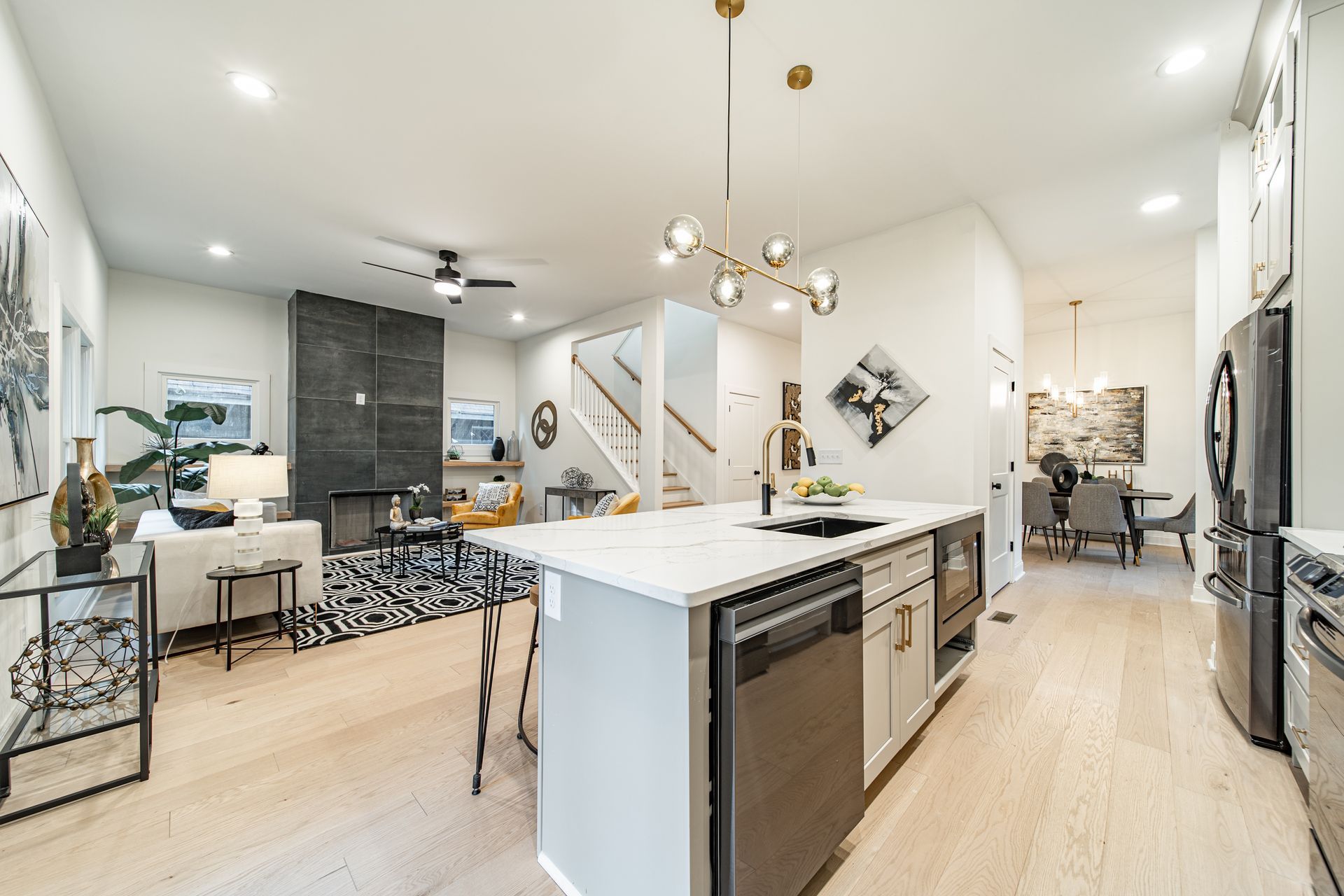 Open-concept kitchen and living area with island, stairs, and dining room; modern decor with light wood floors.