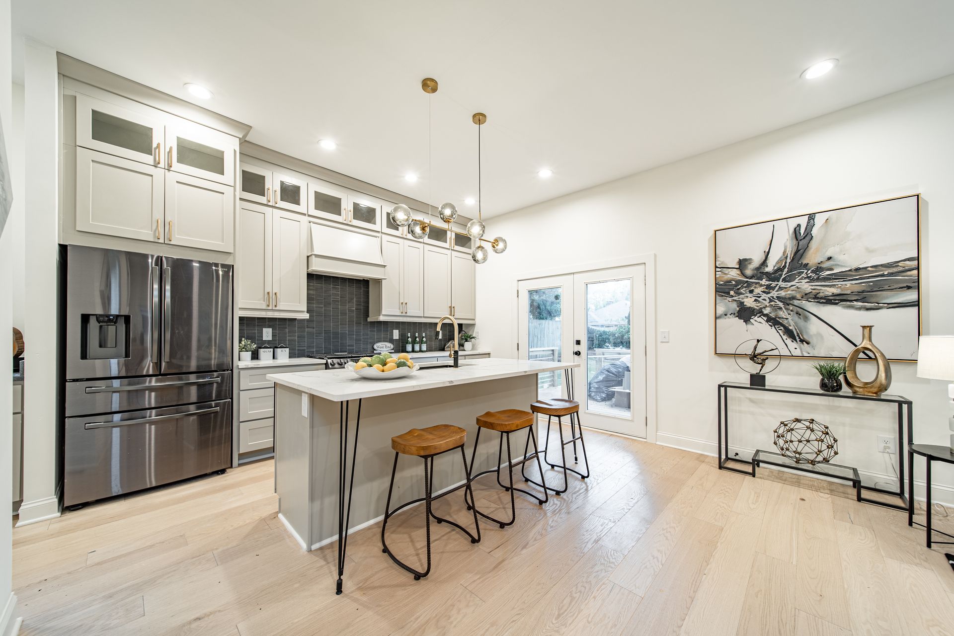 Modern kitchen with white cabinets, stainless steel appliances, island with stools, and light wood flooring.