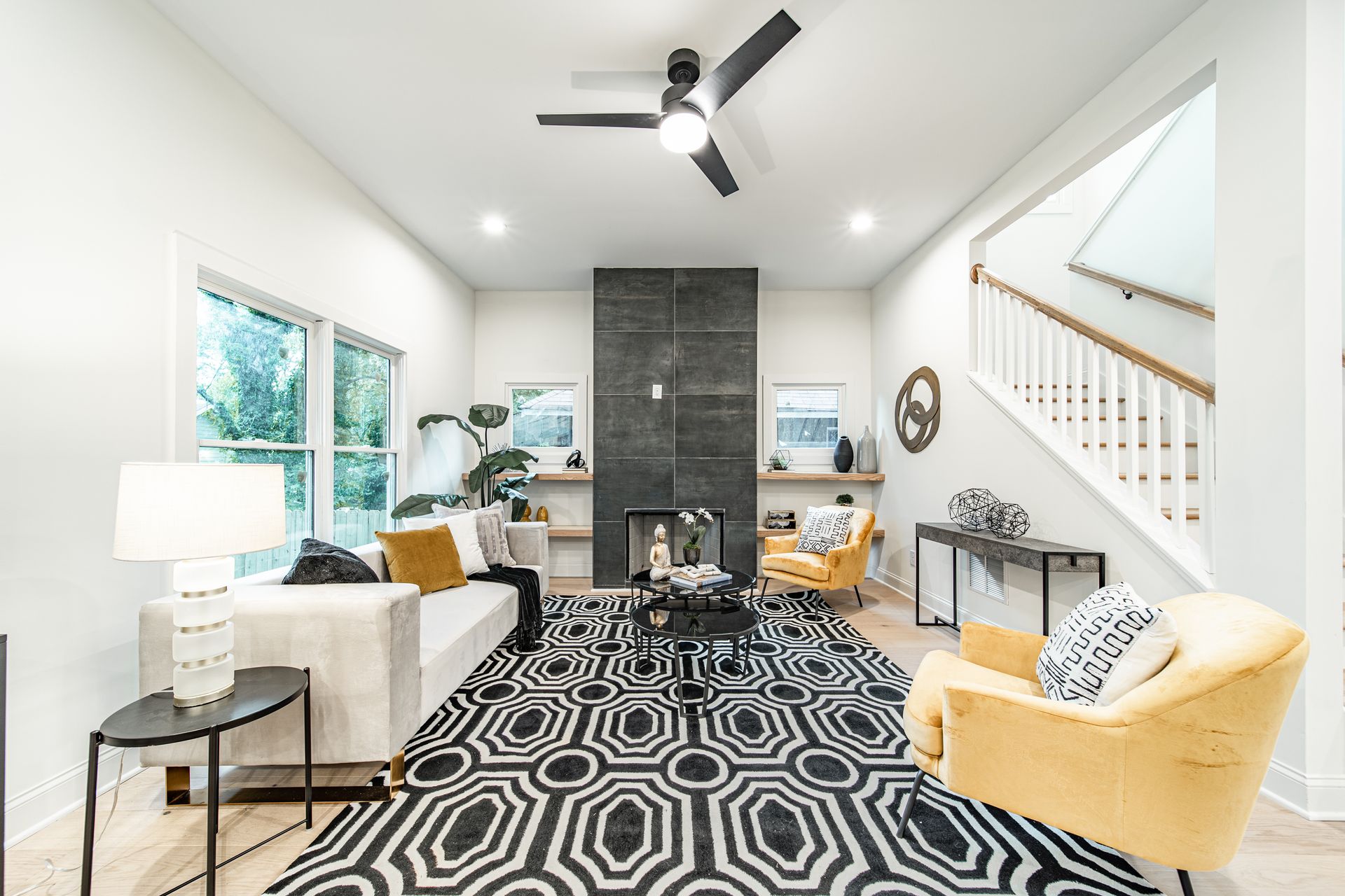 Modern living room with black and white patterned rug, yellow accent chairs, and a fireplace.