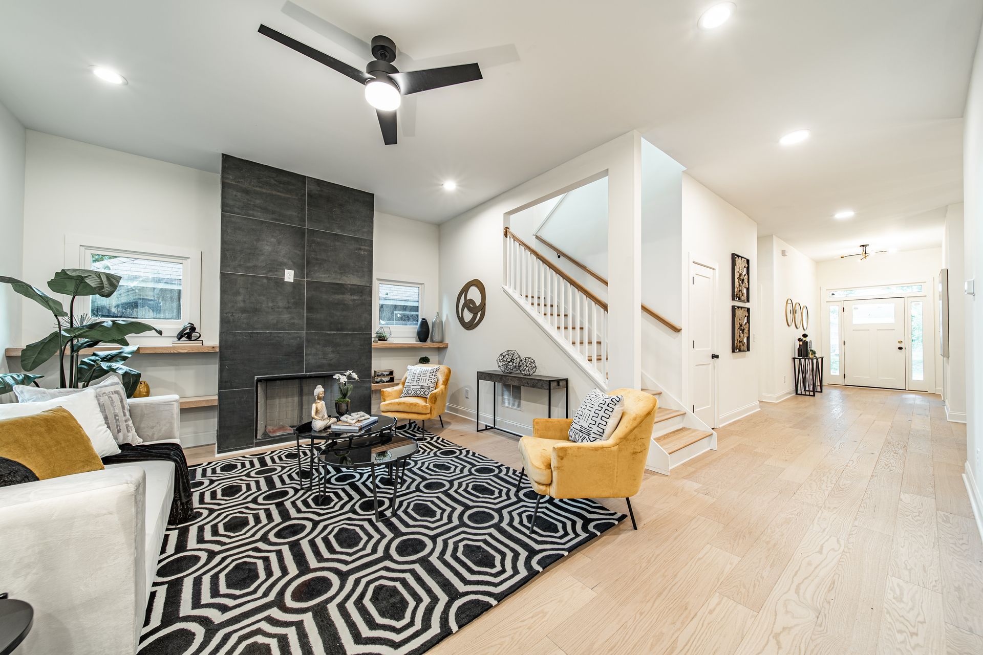 Living room with black fireplace, yellow chairs, geometric rug, and staircase.