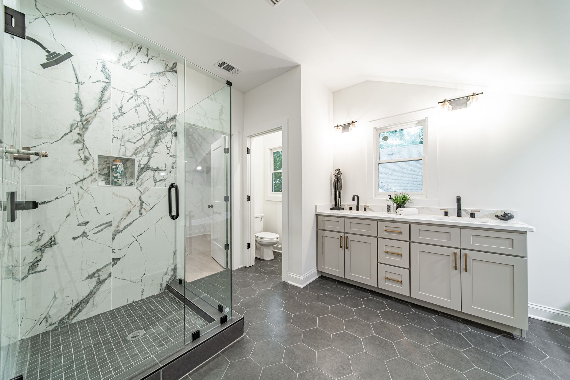 Modern bathroom with large marble-look shower, gray floor, double vanity, and a window.