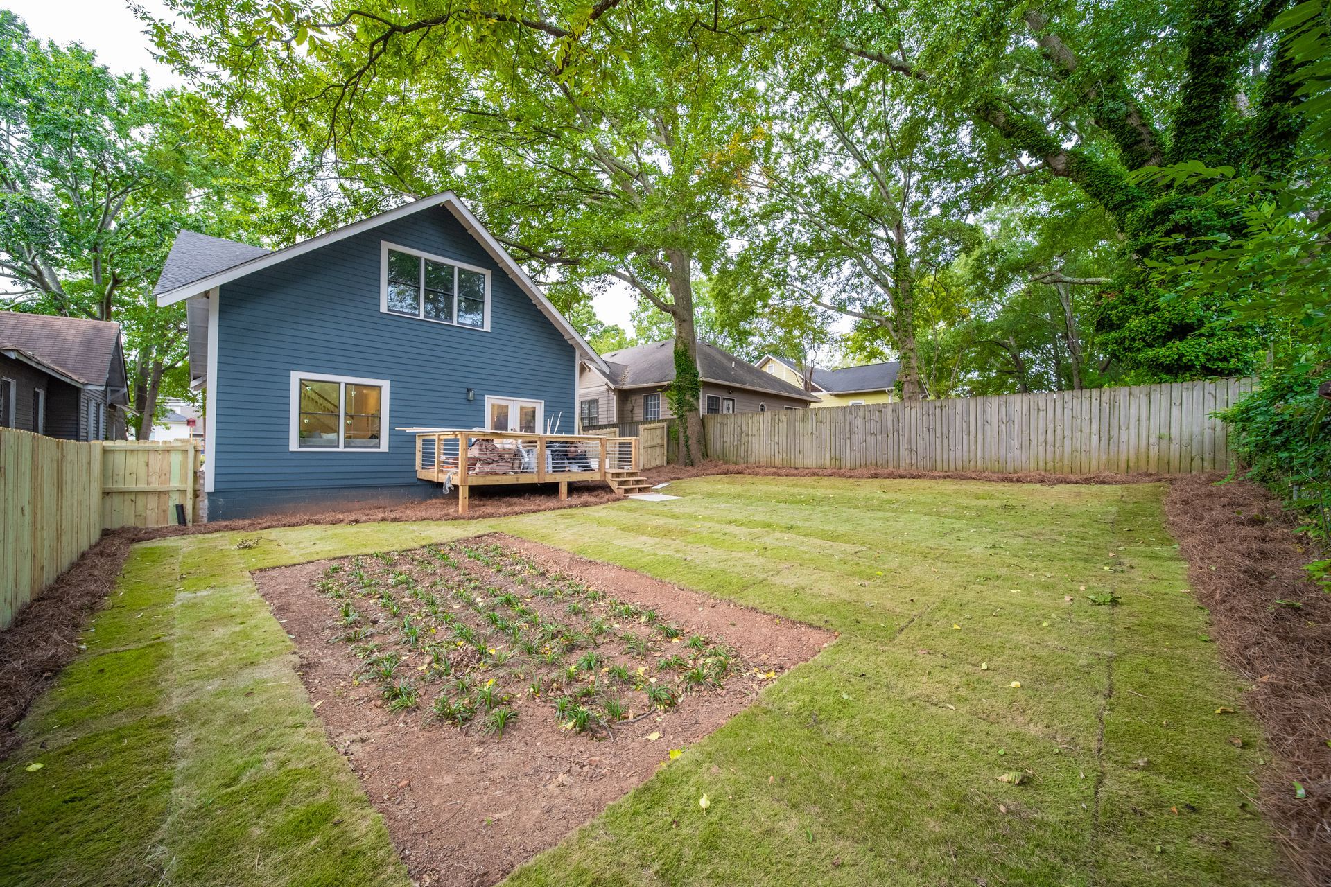 Backyard with blue house, wooden deck, garden bed, and a wooden fence.