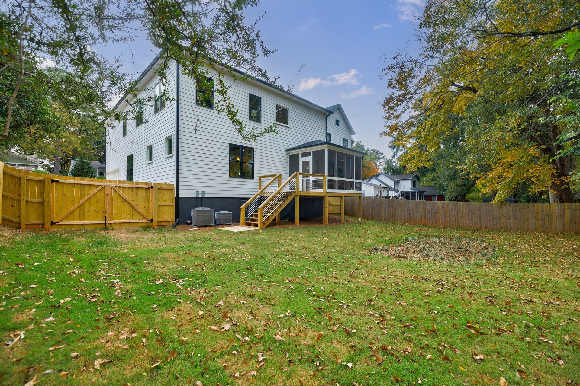 White house with a screened porch and wooden deck; yellow wooden fence on the left; green backyard.