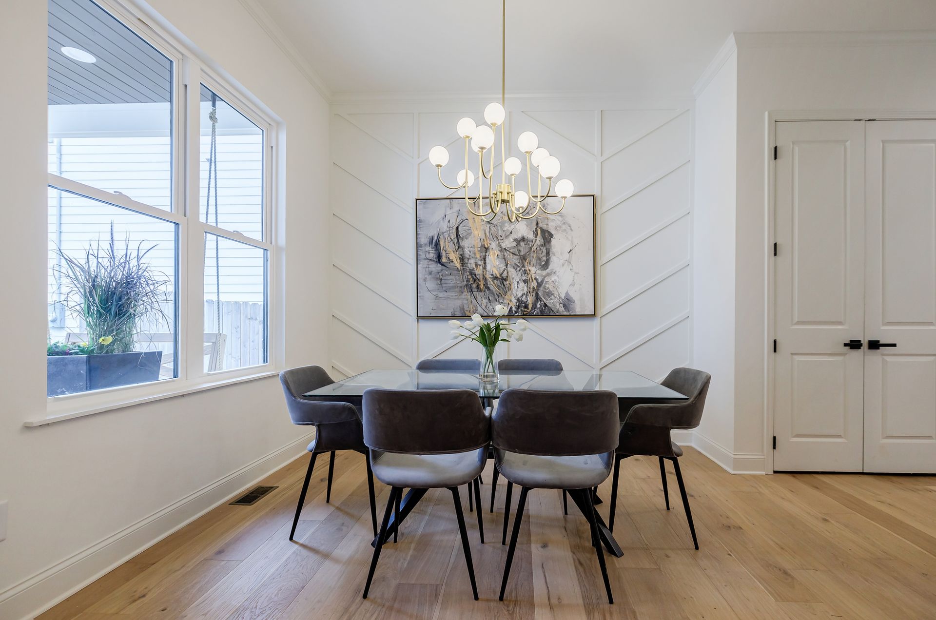 Dining room with table, chairs, art, and light fixture against a white chevron wall.