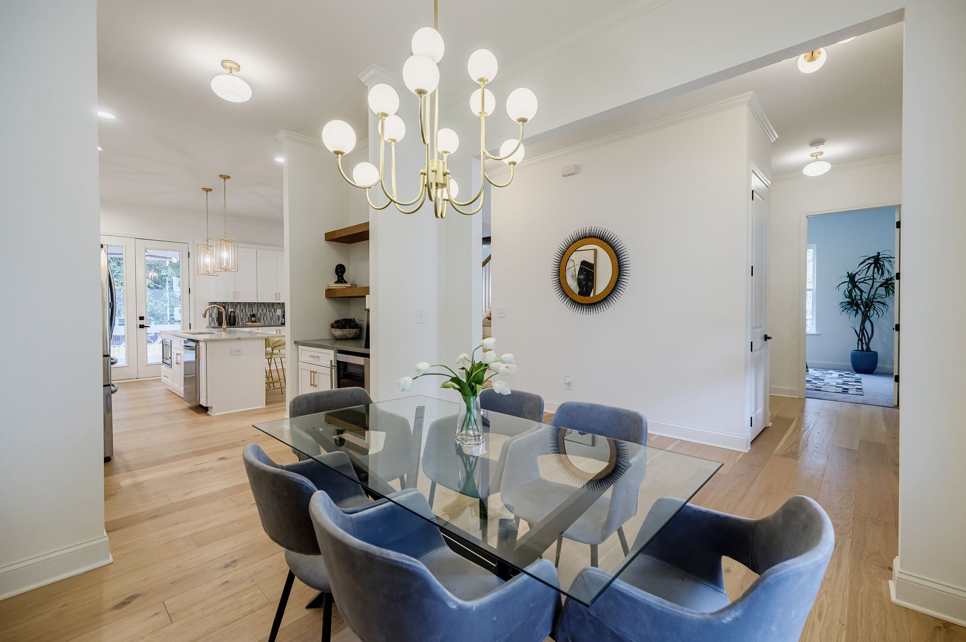 Dining room with glass table and gray chairs, gold chandelier.