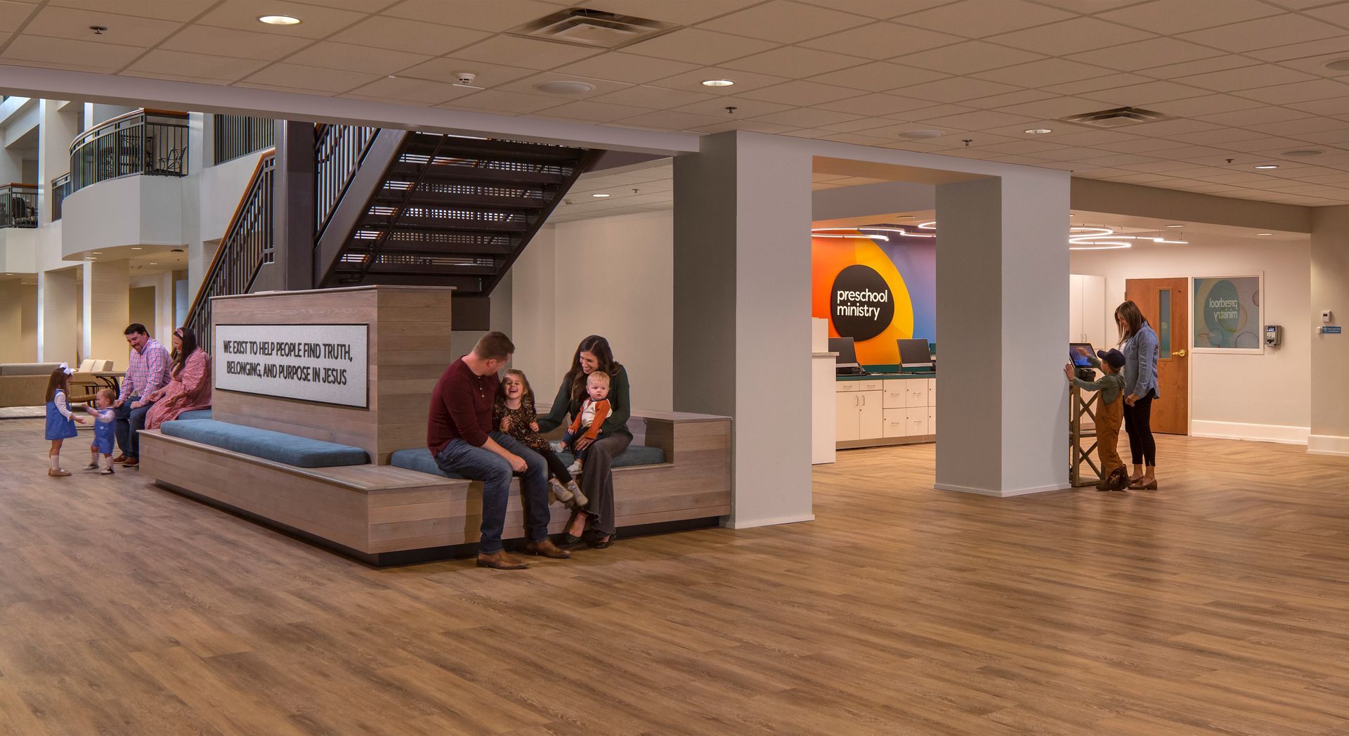 People sit on a bench in an open lobby with a staircase and a reception desk.