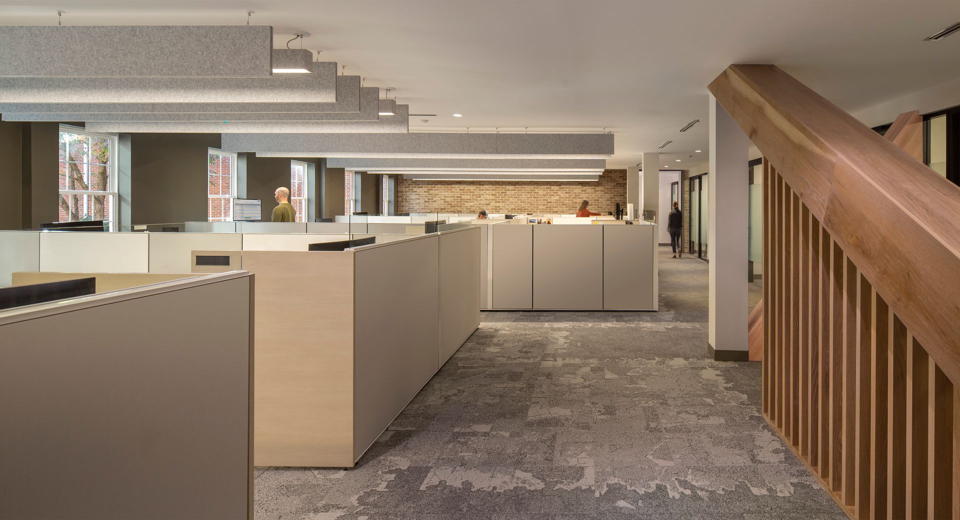 Office interior with cubicles, neutral colors, and a wooden staircase.