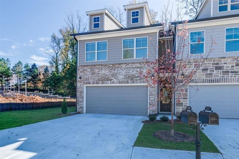 Townhouse exterior with grey siding, brick, two-car garage, and dormers. Concrete driveway and small lawn.