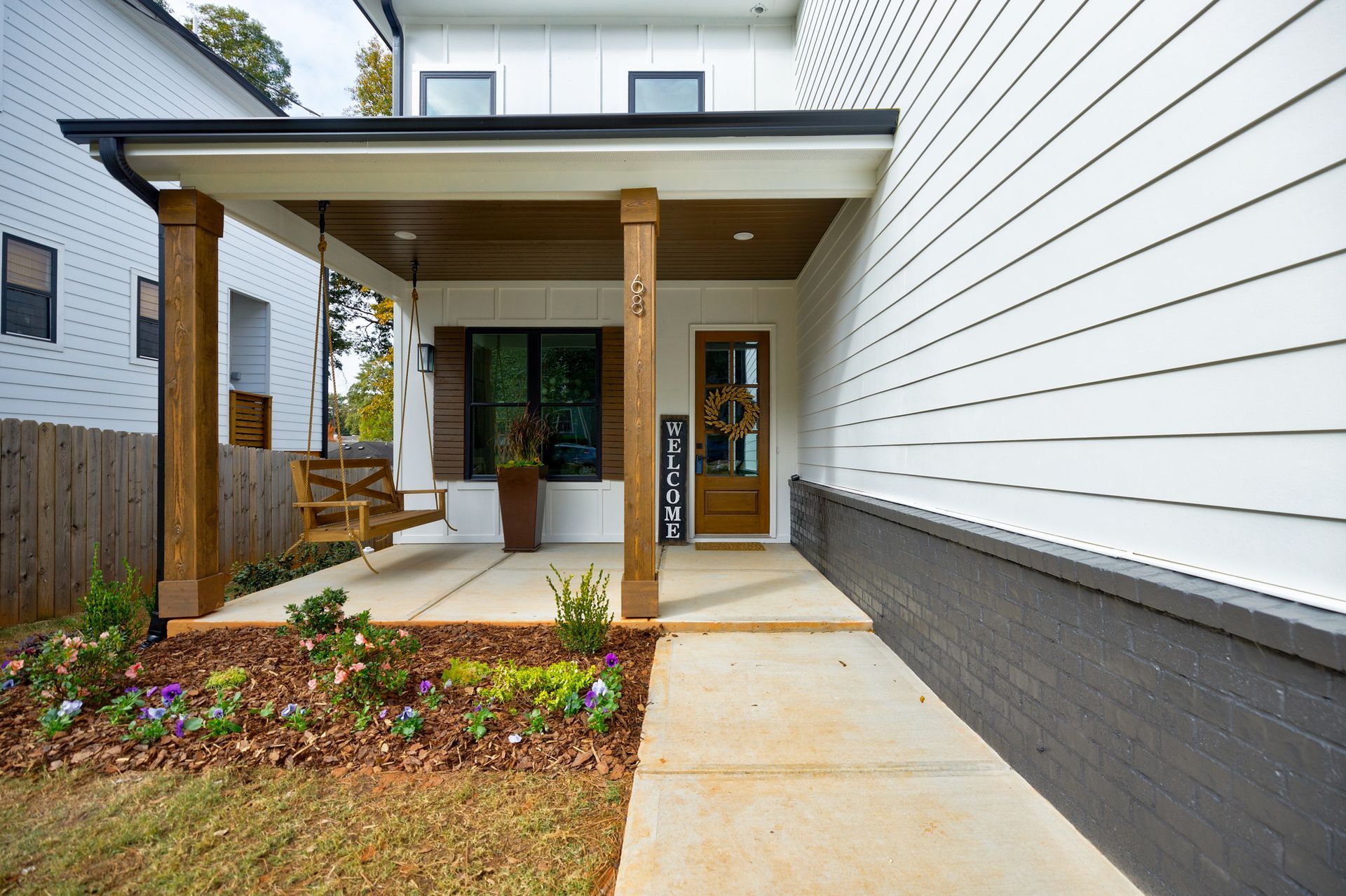White house with brown porch posts and door, swing, and flower bed.