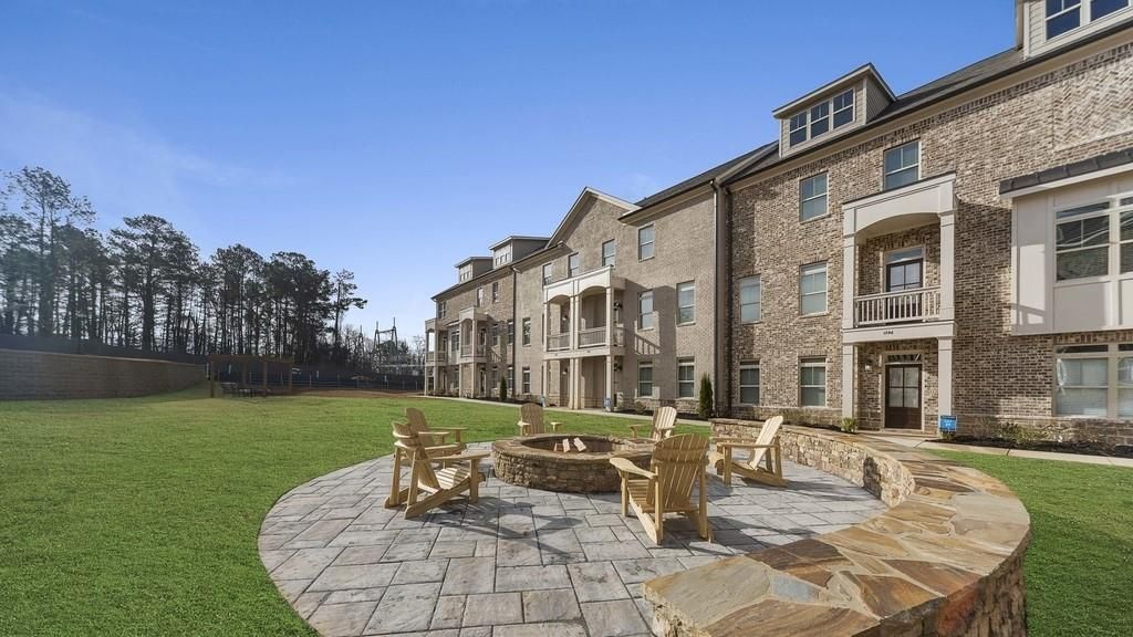 Stone building with fire pit and chairs on a grassy lawn under a clear blue sky.
