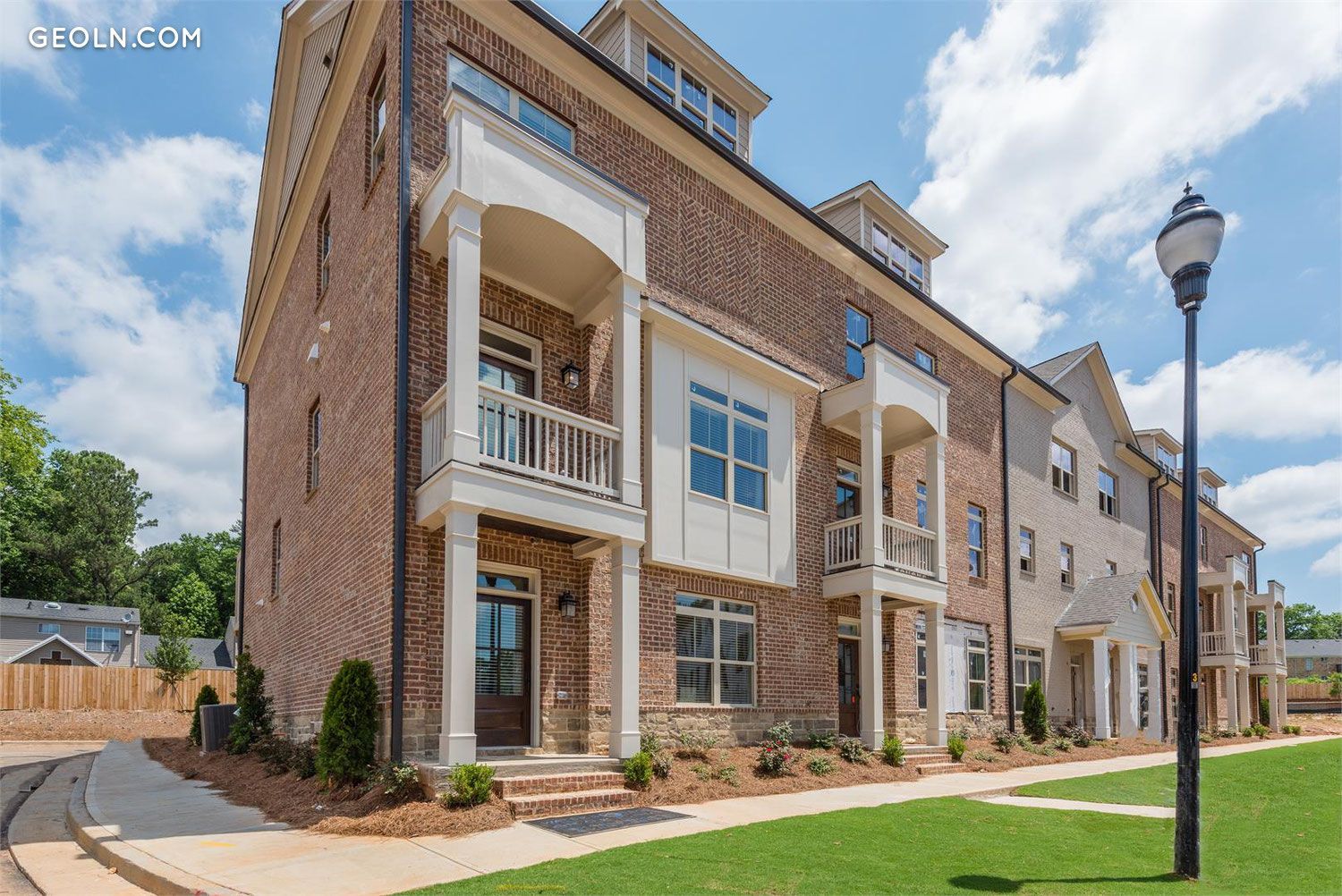 Multi-story brick townhouses with white trim and balconies, under a partly cloudy sky.