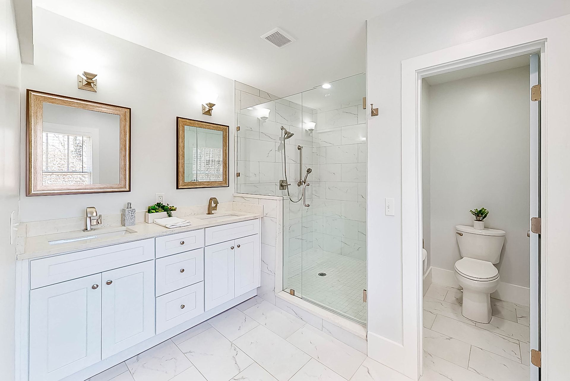 White bathroom with a double sink vanity, glass shower, and toilet room.