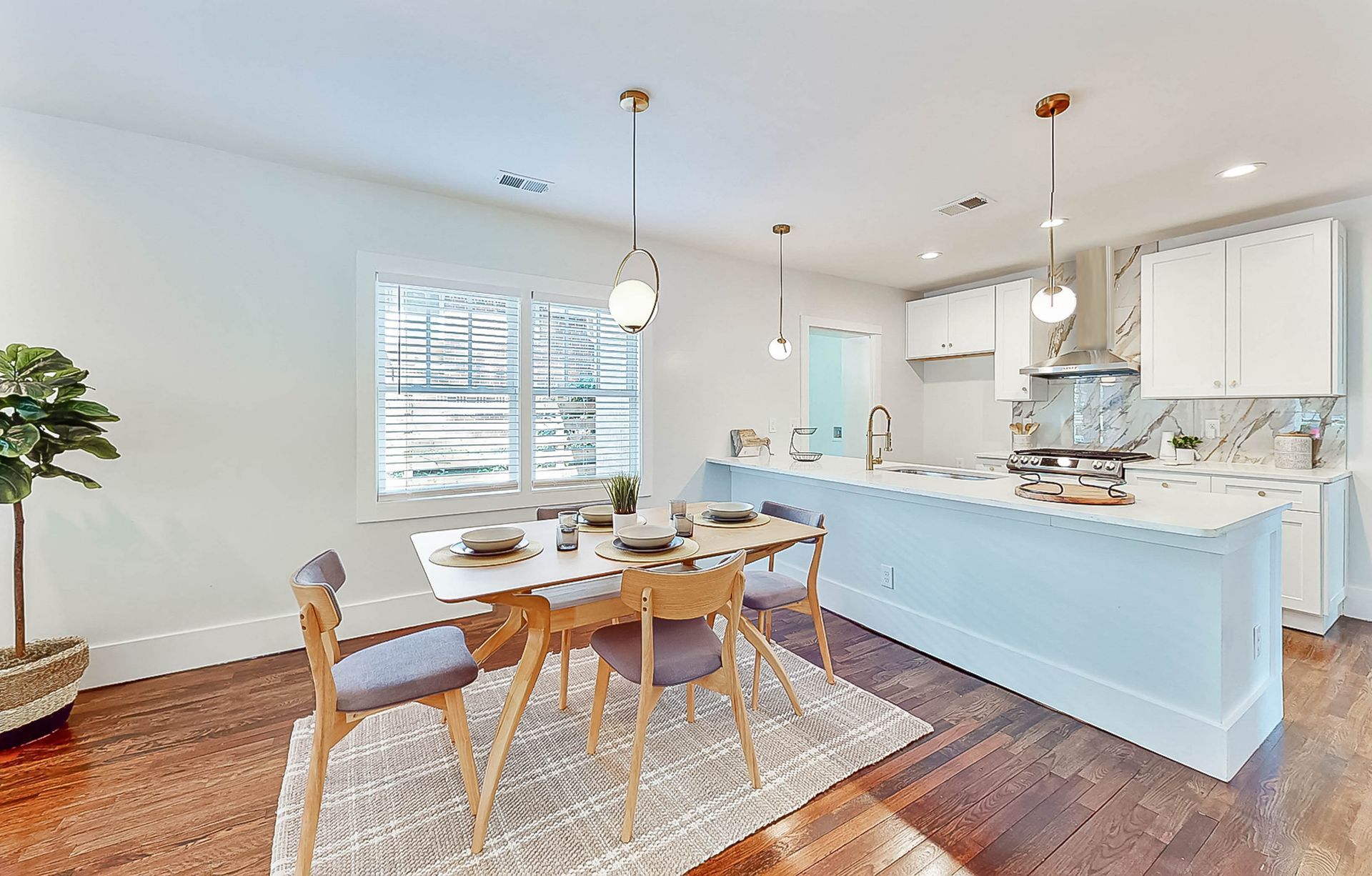 Dining area with kitchen: white cabinets, island, table set for four, wood floor, natural light.