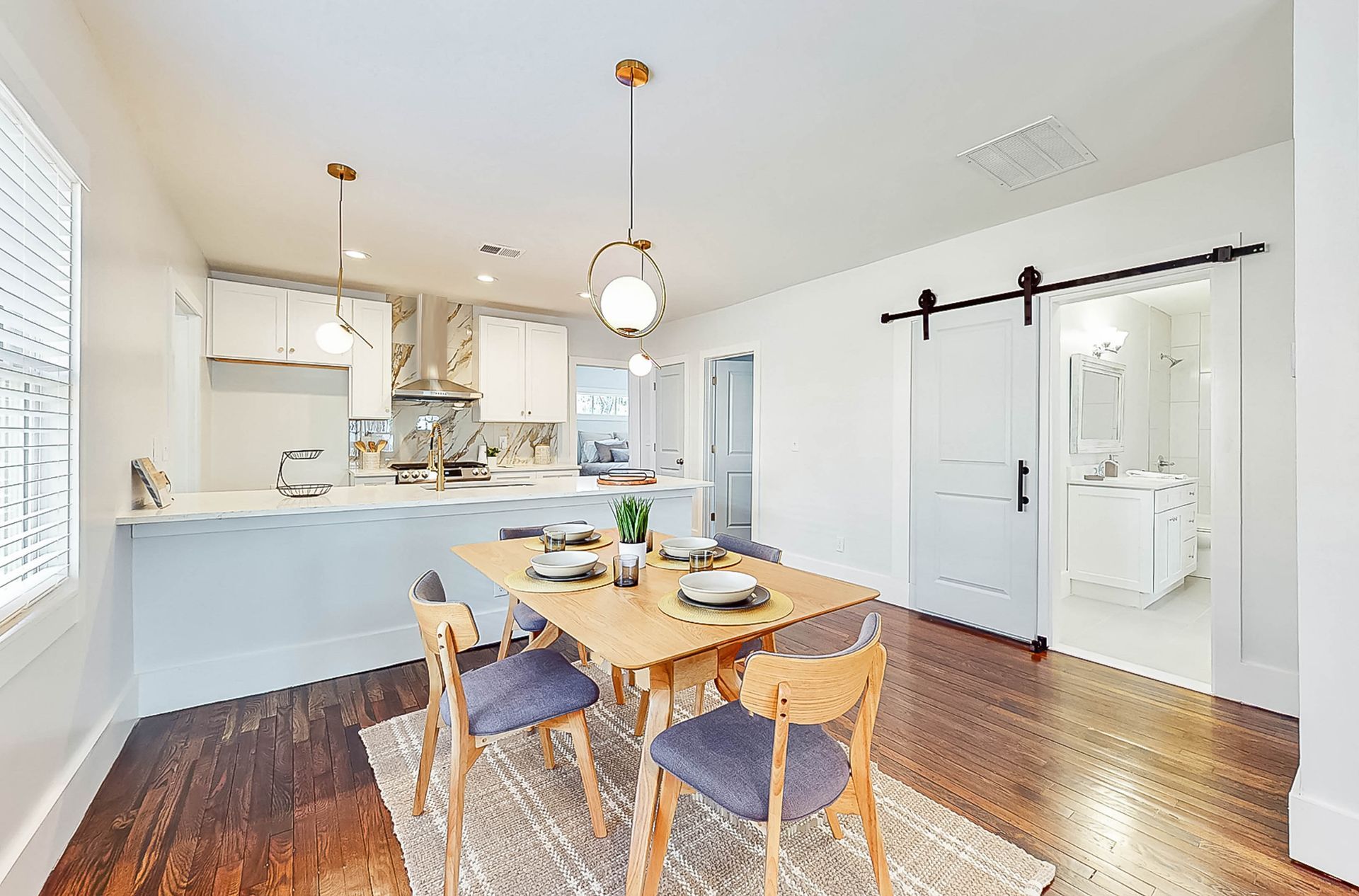 Dining area with wooden table, blue chairs, open kitchen, sliding door to bathroom.