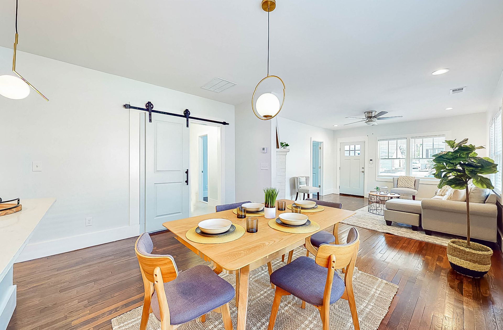 Dining room with wood table, chairs, and hanging light. Open to living room with sofa, rug, and window.