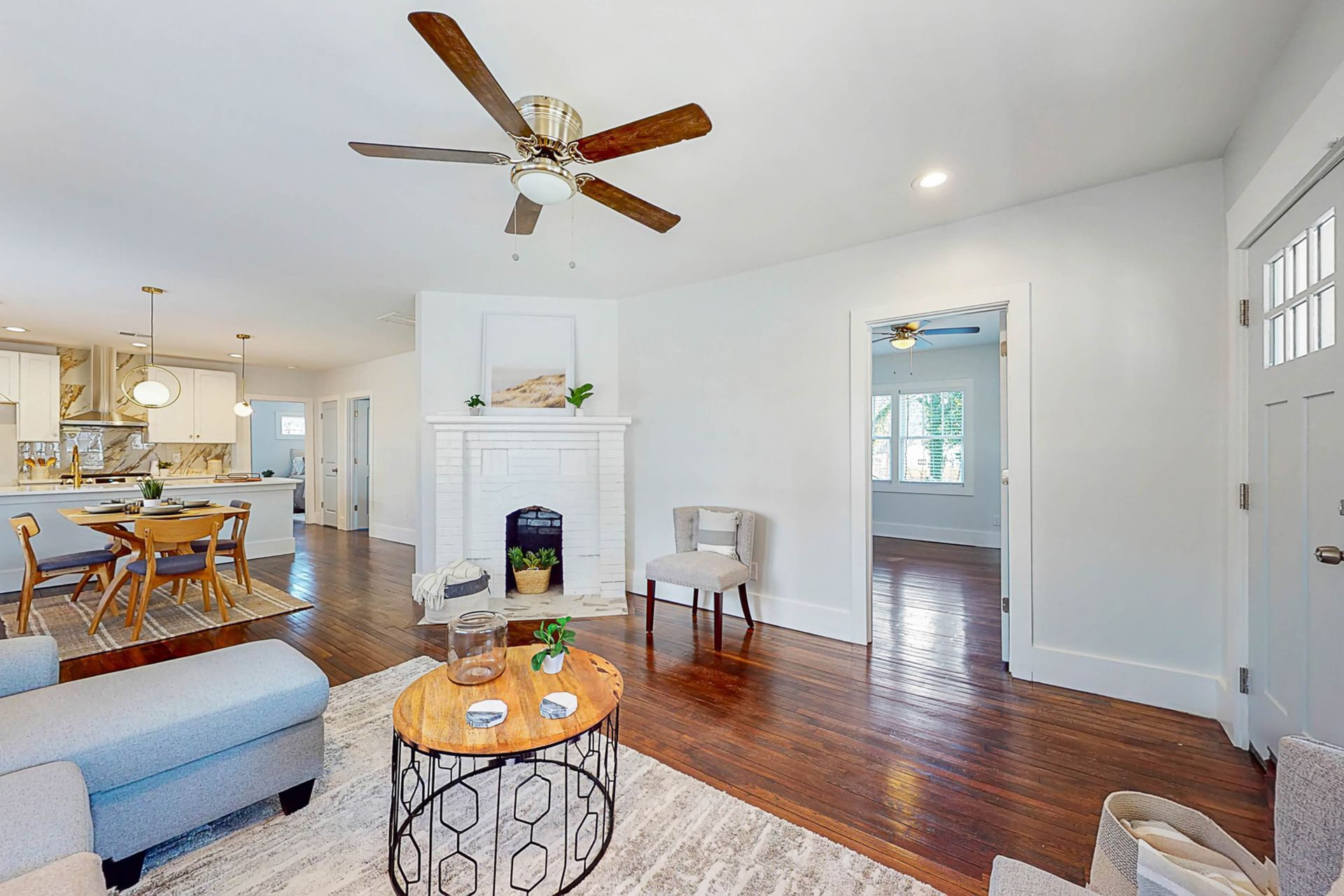 Living room with hardwood floors, fireplace, and open view to kitchen and doorway.