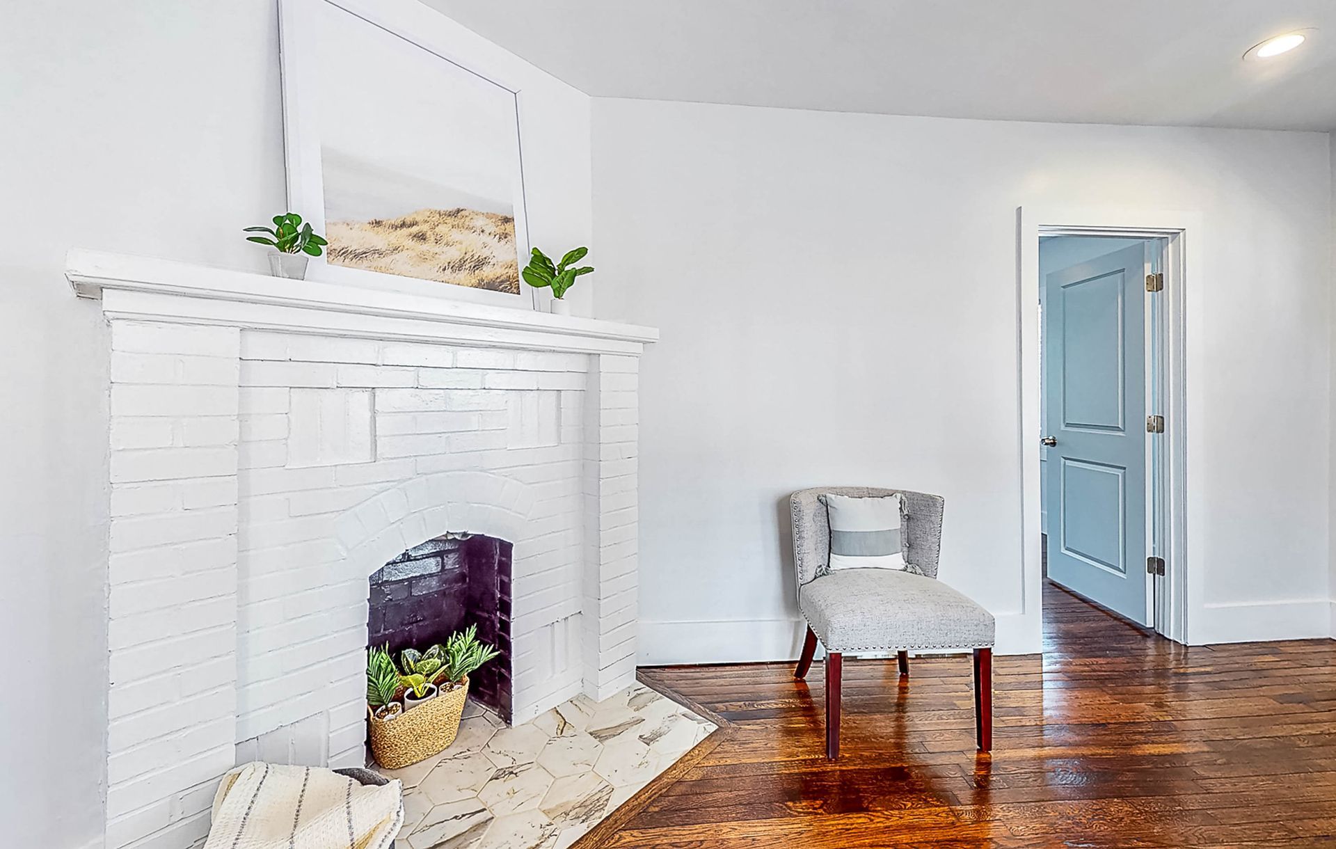 White-painted fireplace with mirror, potted plants, a patterned rug, and a light blue door in a room.