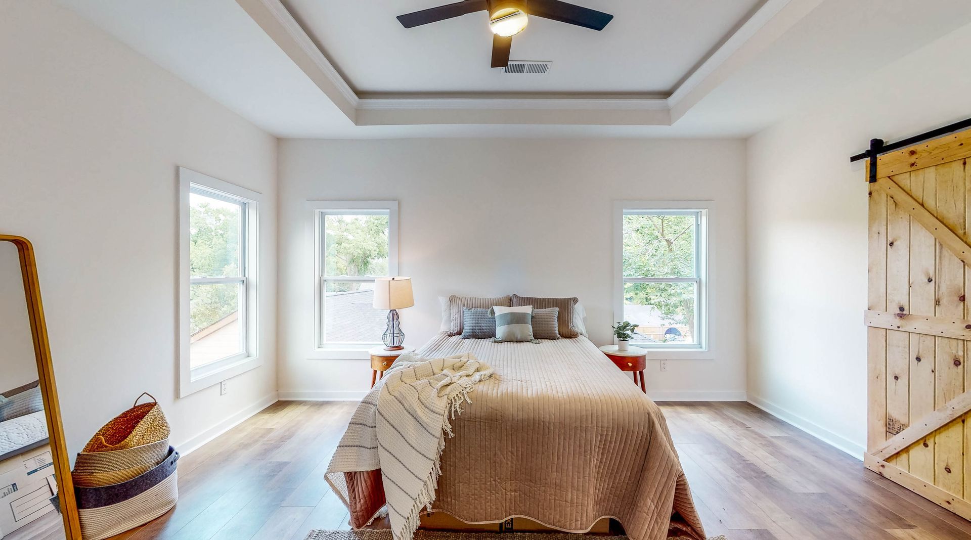 Bedroom with wooden floor, bed, windows, ceiling fan, and sliding barn door.