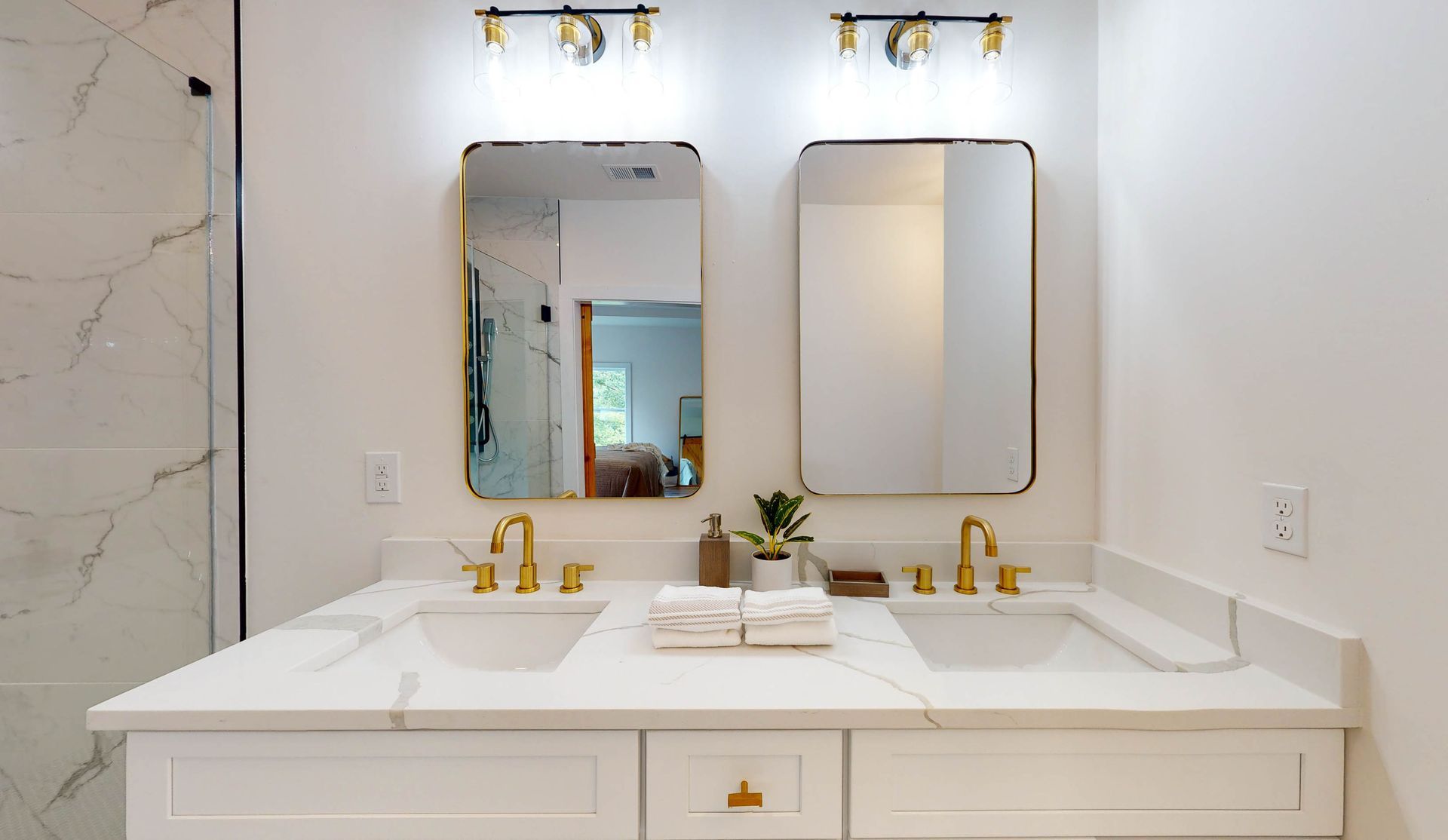 Bathroom with white marble countertop, two sinks, mirrors, and gold fixtures.