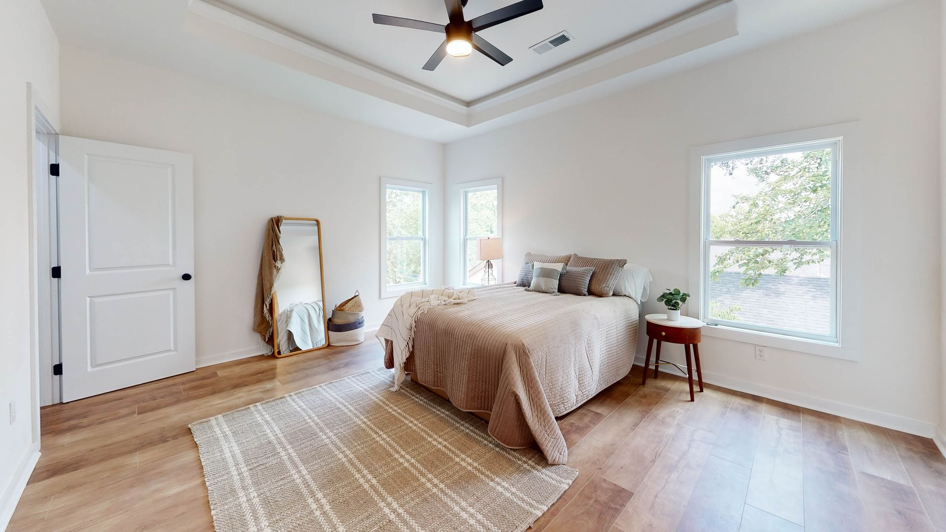 Bedroom with a bed, rug, mirror, and two windows. Neutral tones and wood flooring.