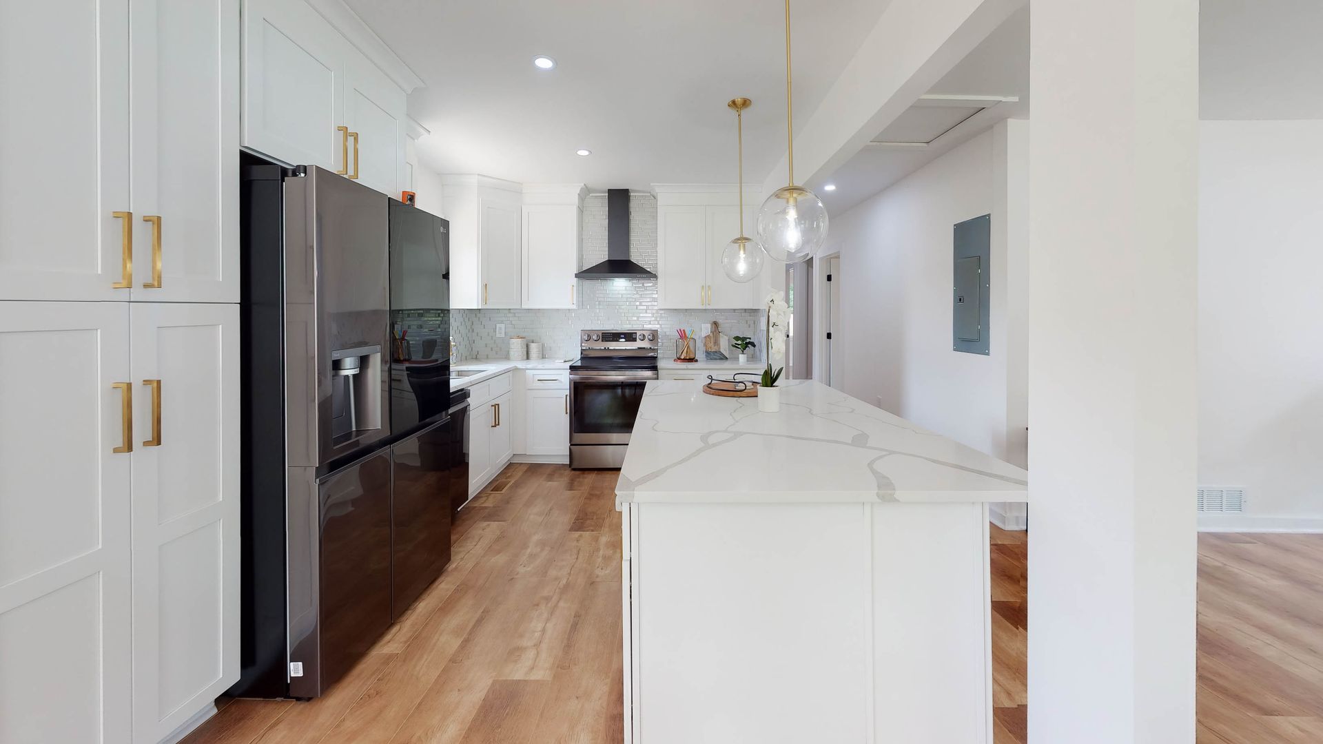 Modern white kitchen with a black refrigerator, island, and wood floors.
