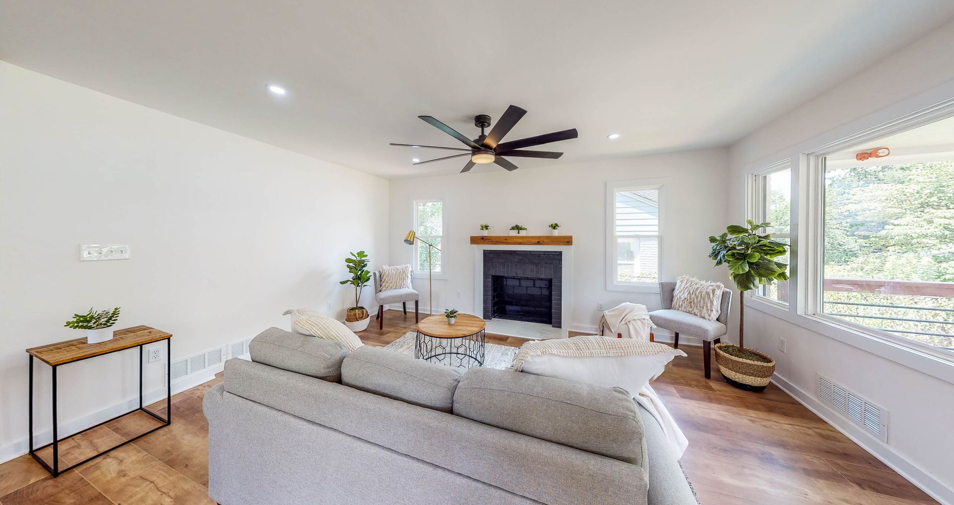 Spacious living room with fireplace, sofa, and large windows. Warm wood floors and neutral walls.