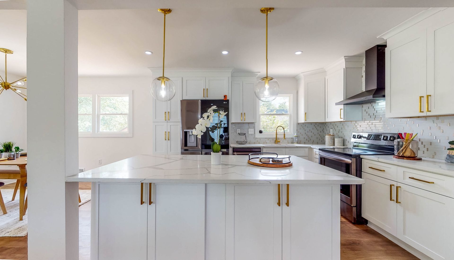 White kitchen with island, marble countertops, gold hardware, and pendant lights.
