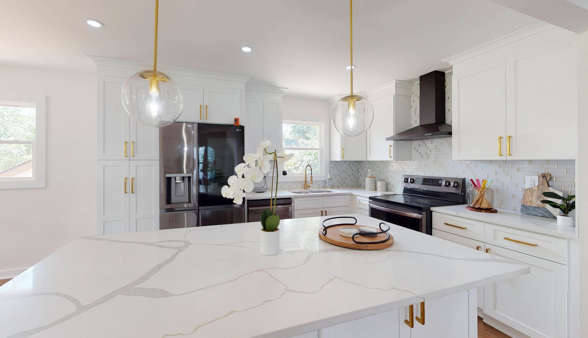 Bright, modern kitchen with white cabinets, large island, gold hardware, and a black range hood.