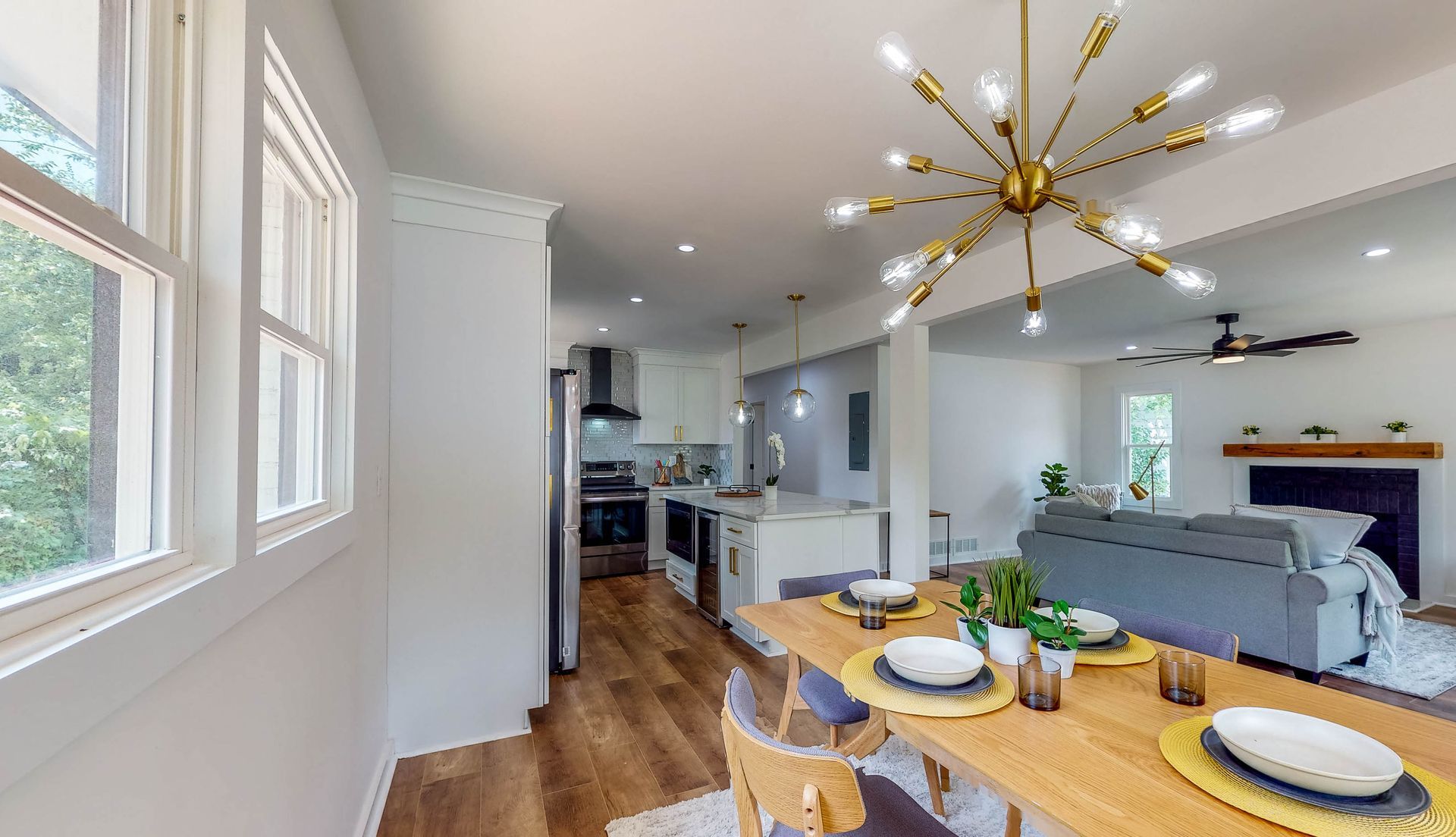 Dining room and kitchen. Dining table set for a meal. Kitchen has white cabinets and stainless steel appliances.