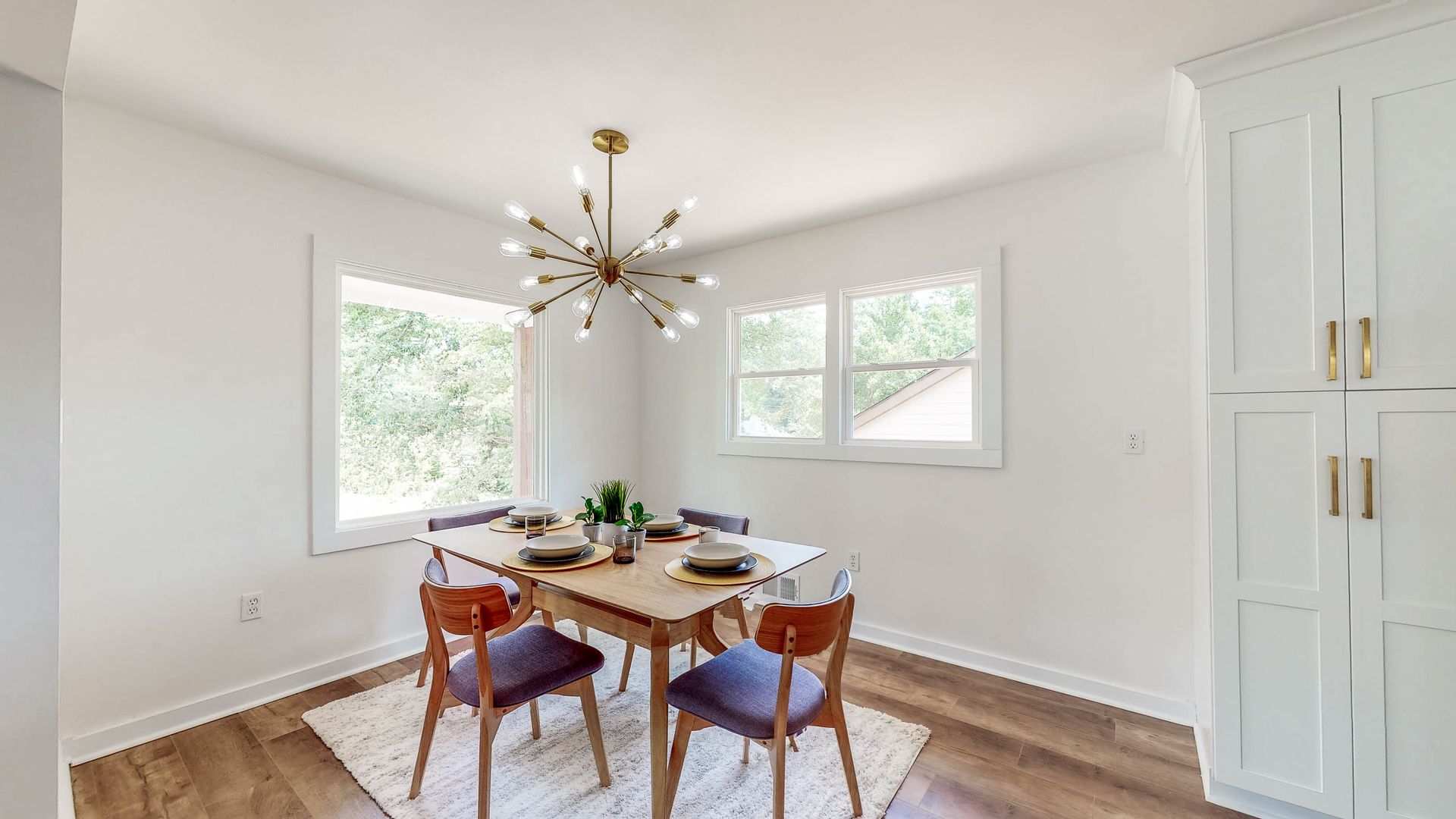 Dining room with a table, chairs, windows, and a chandelier. White walls and hardwood floors.