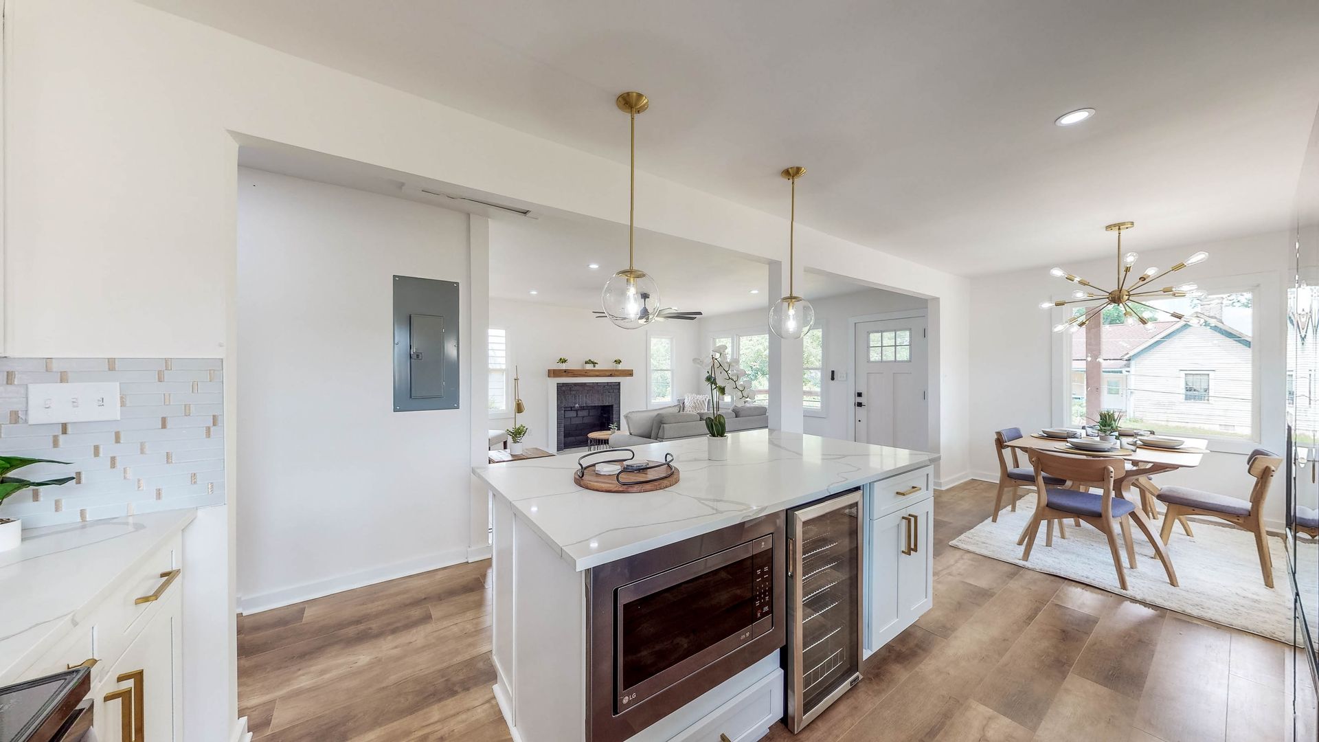 Modern kitchen with island, marble countertops, and wine fridge. Dining area and living room visible.