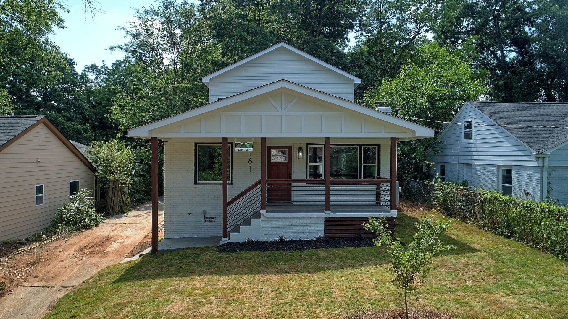 White two-story house with porch. Dark brown railing, red door, and trees in background.