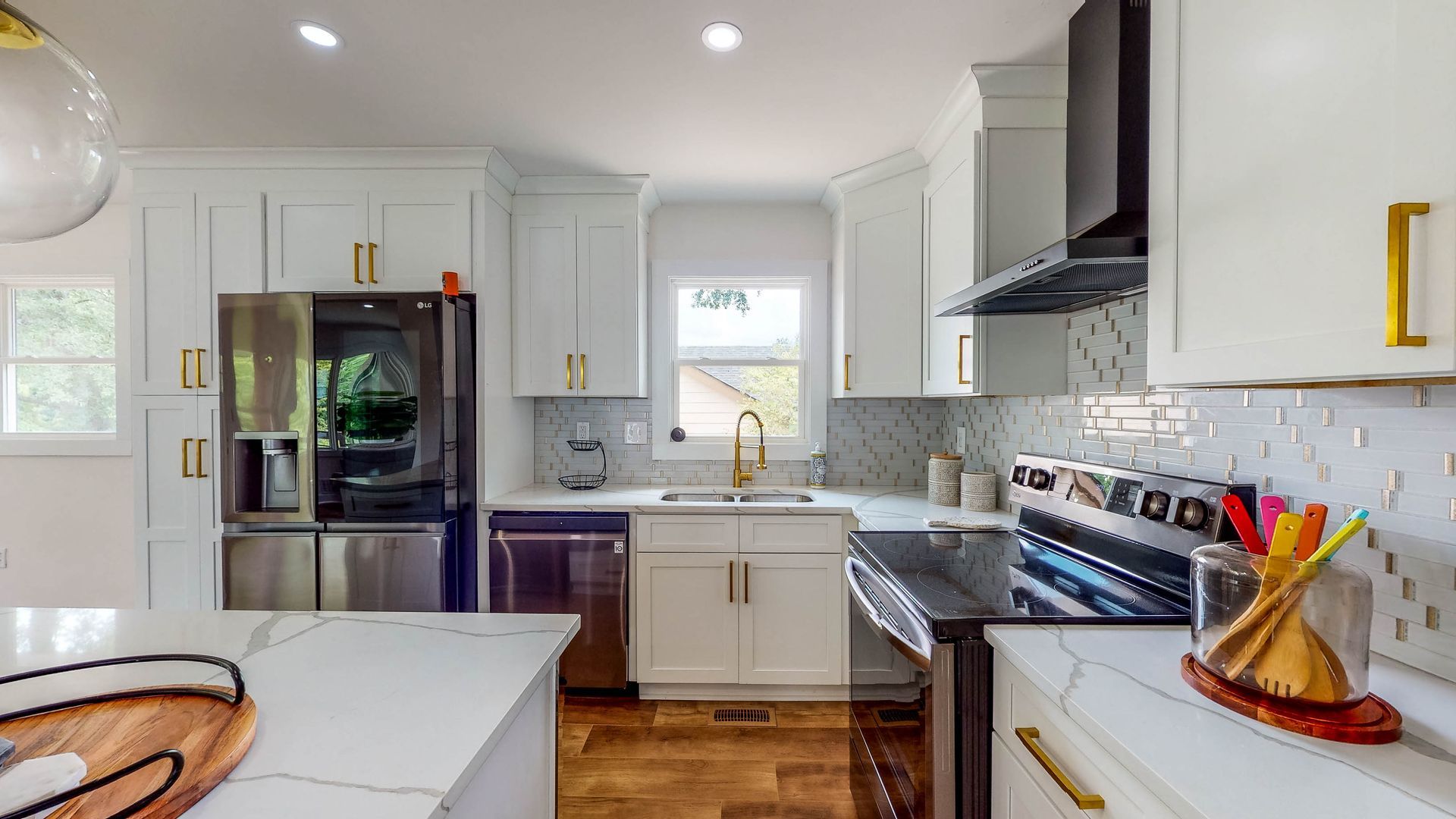 Modern kitchen with white cabinets, gold hardware, stainless steel appliances, and a marble countertop.