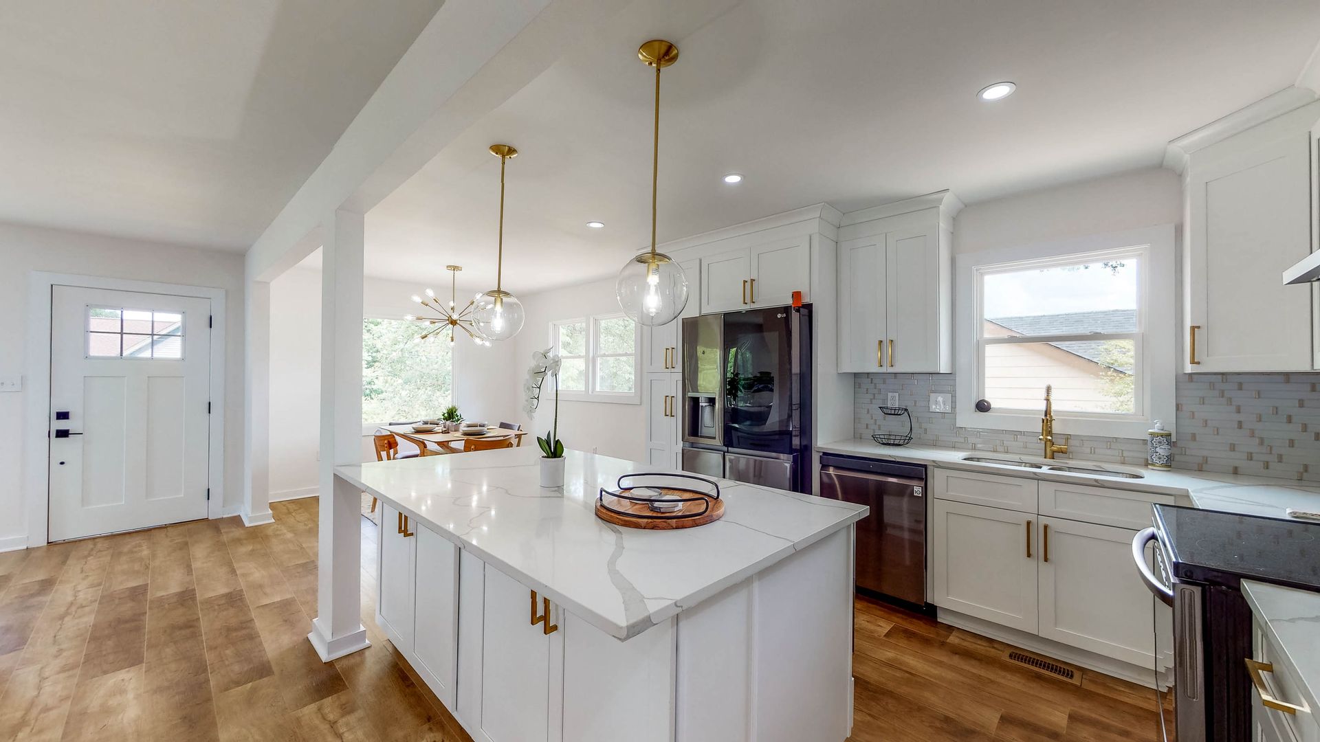 Modern white kitchen with island, gold hardware, open to dining area, hardwood floors.