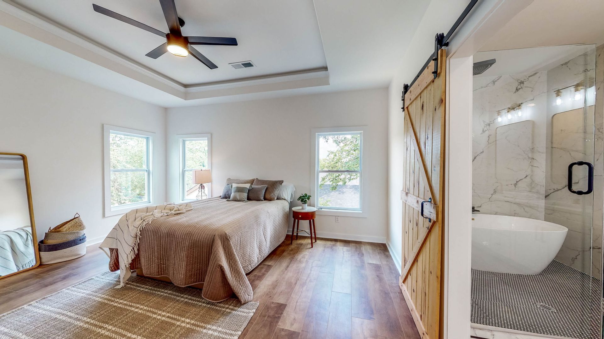 Bedroom with bed, windows, wooden floor, and a bathroom with a sliding barn door.