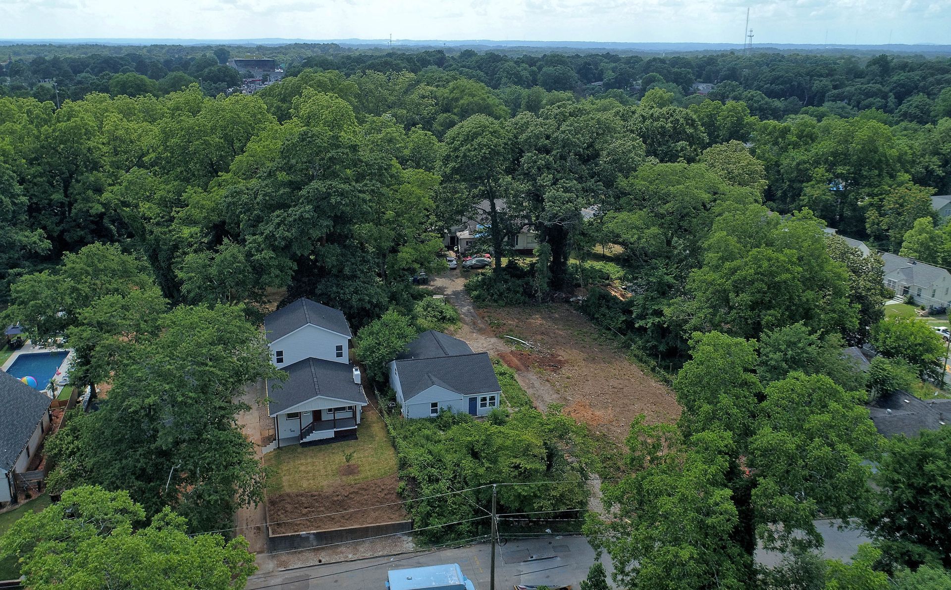 Aerial view of neighborhood houses surrounded by trees; a cleared lot is visible.